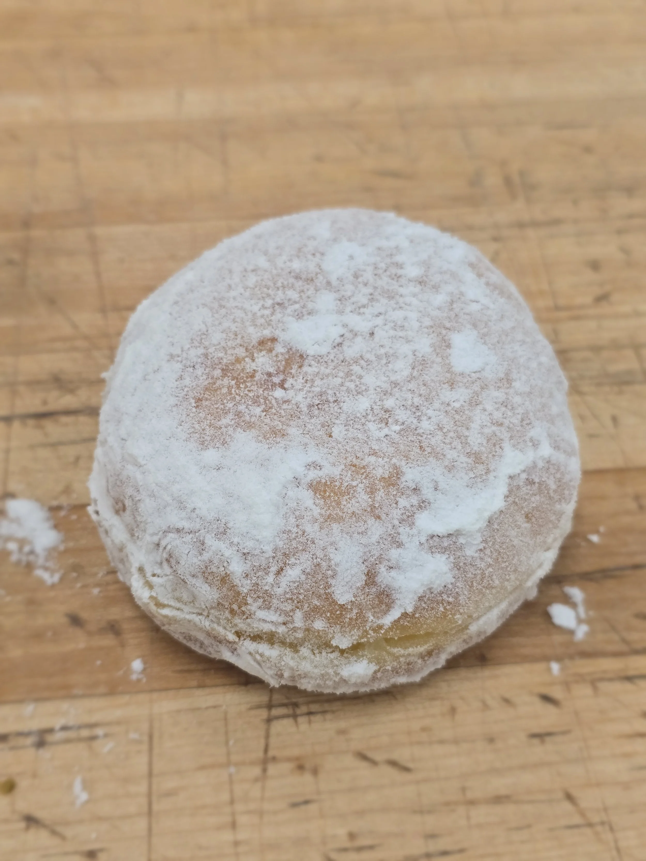 A round powdered donut on a wooden surface.