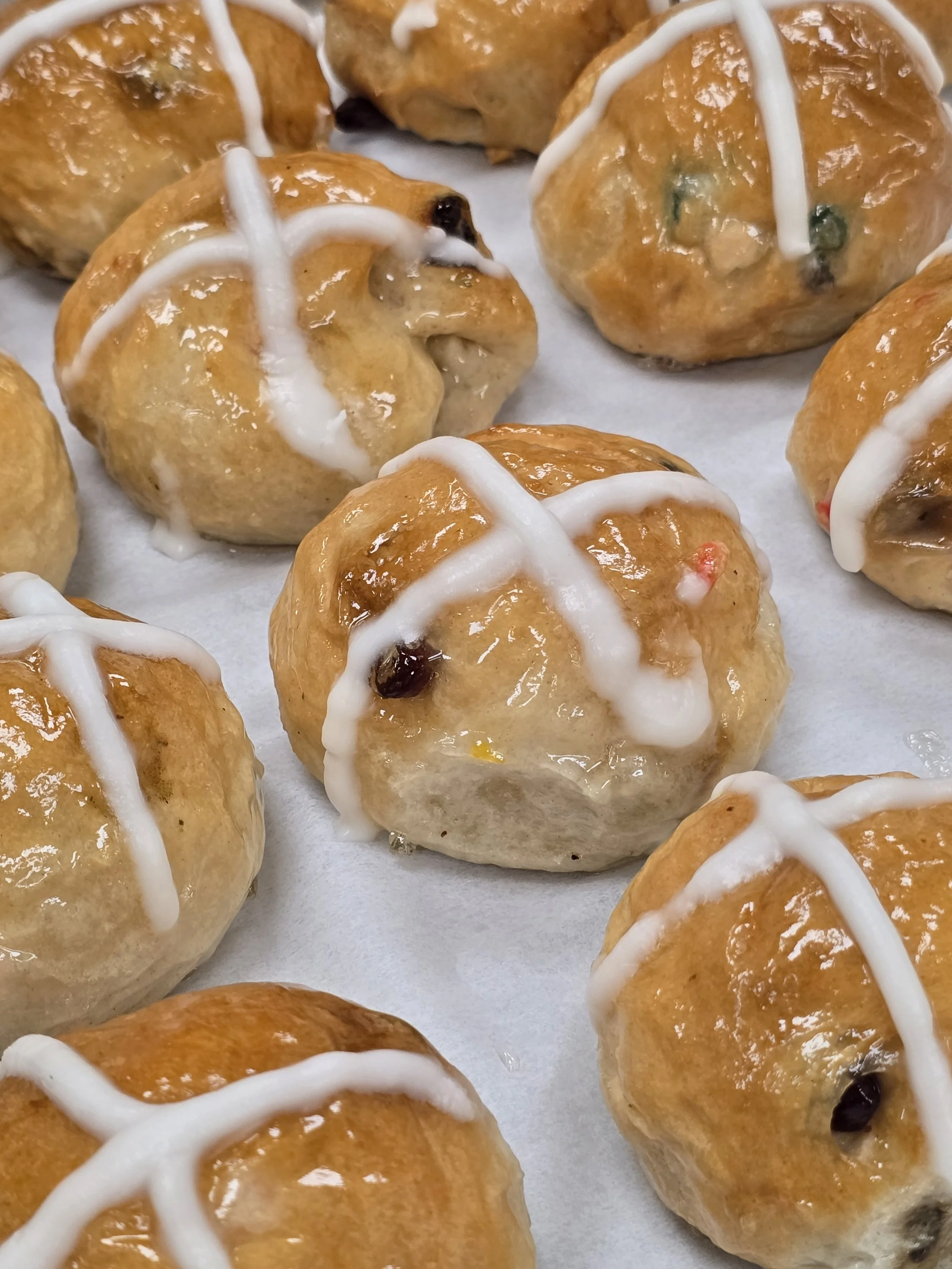 Close-up of freshly baked cinnamon rolls drizzled with white icing, placed on parchment paper.