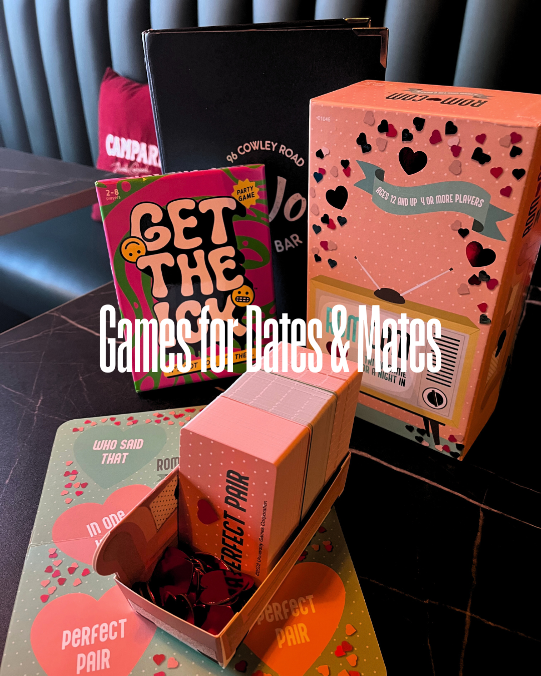 A collection of Valentine's Day board games for Dates & Mates with a dark background and a red pillow in the background at JoJo's Cocktail & Pizza Bar, Cowley Road, Oxford.