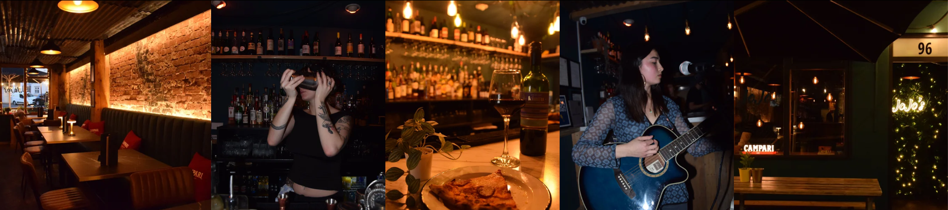 Interior of a cozy bar or restaurant with exposed brick walls, warm lighting, tables, a woman playing guitar, and bar area with bottles and a woman bartender.
