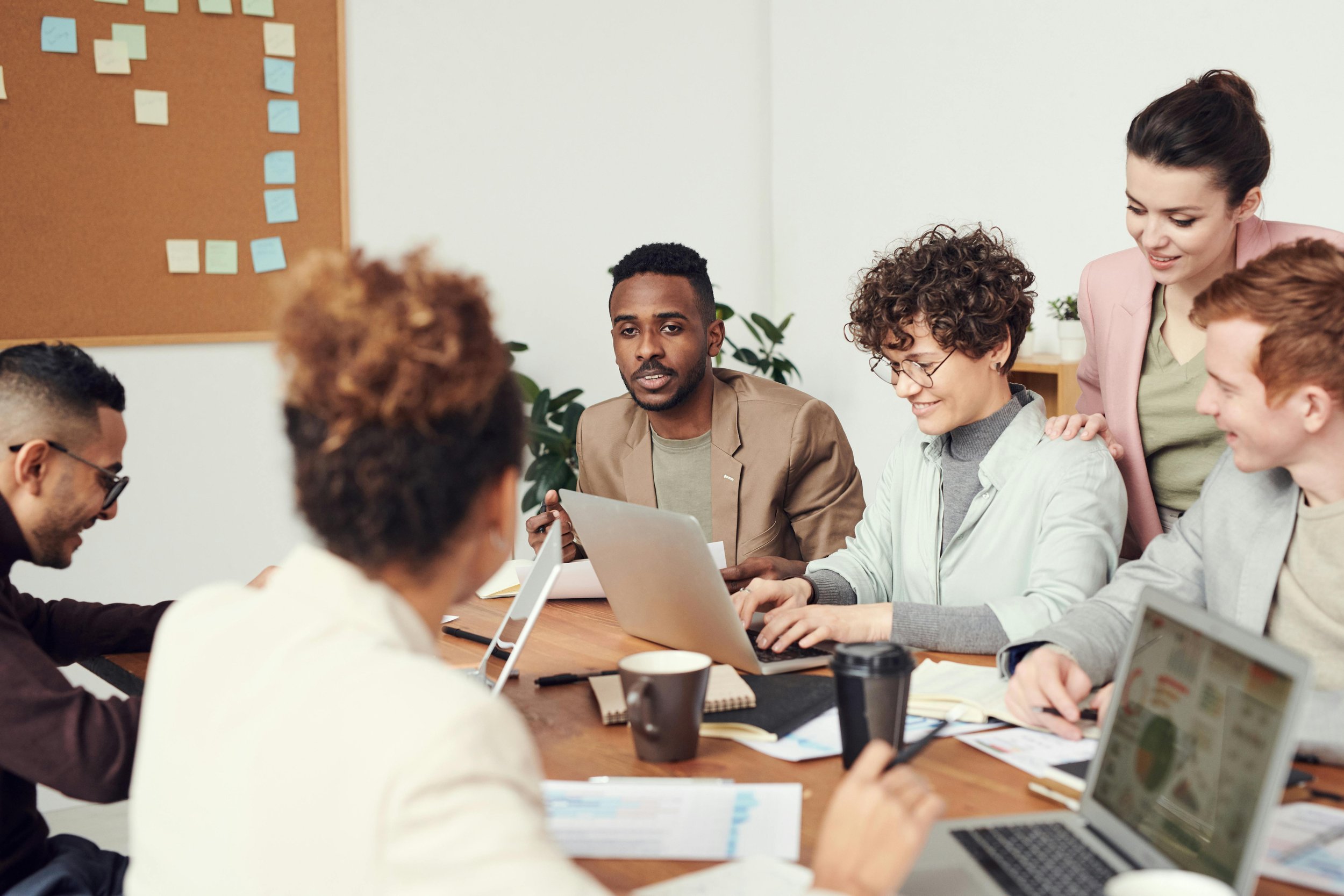 Group of people having a meeting in a conference room, some using laptops, with notes and documents on the table.