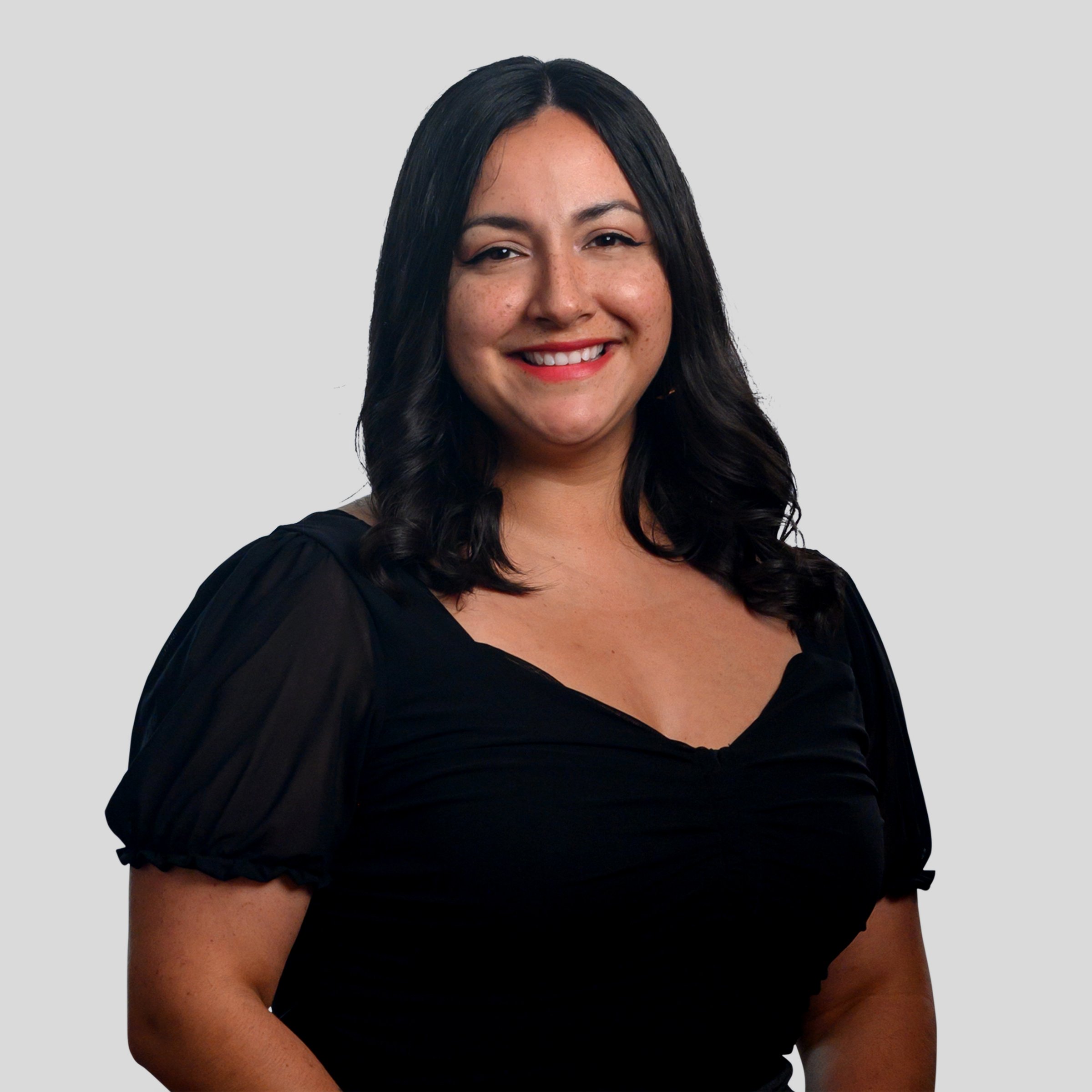A woman with shoulder-length dark hair smiling, wearing a black top with puffy sleeves, against a light gray background.