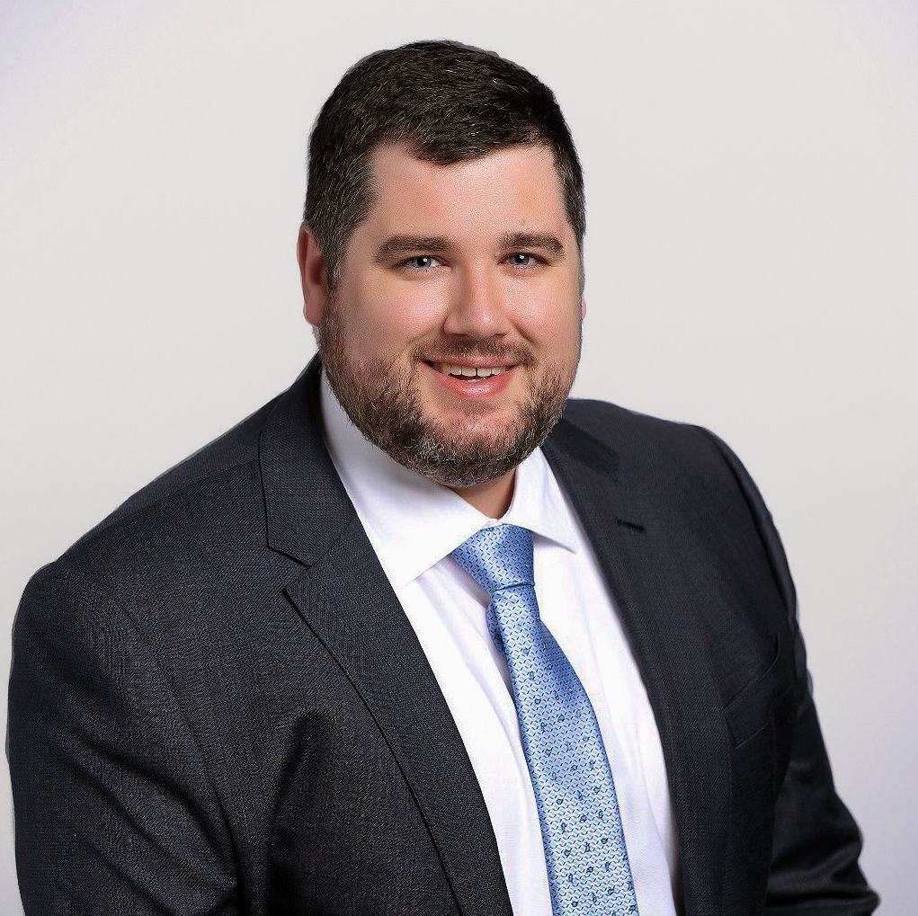 David Henry, attorney. A man with dark hair and beard in a suit, white shirt, and blue tie, smiling at the camera against a plain white background.