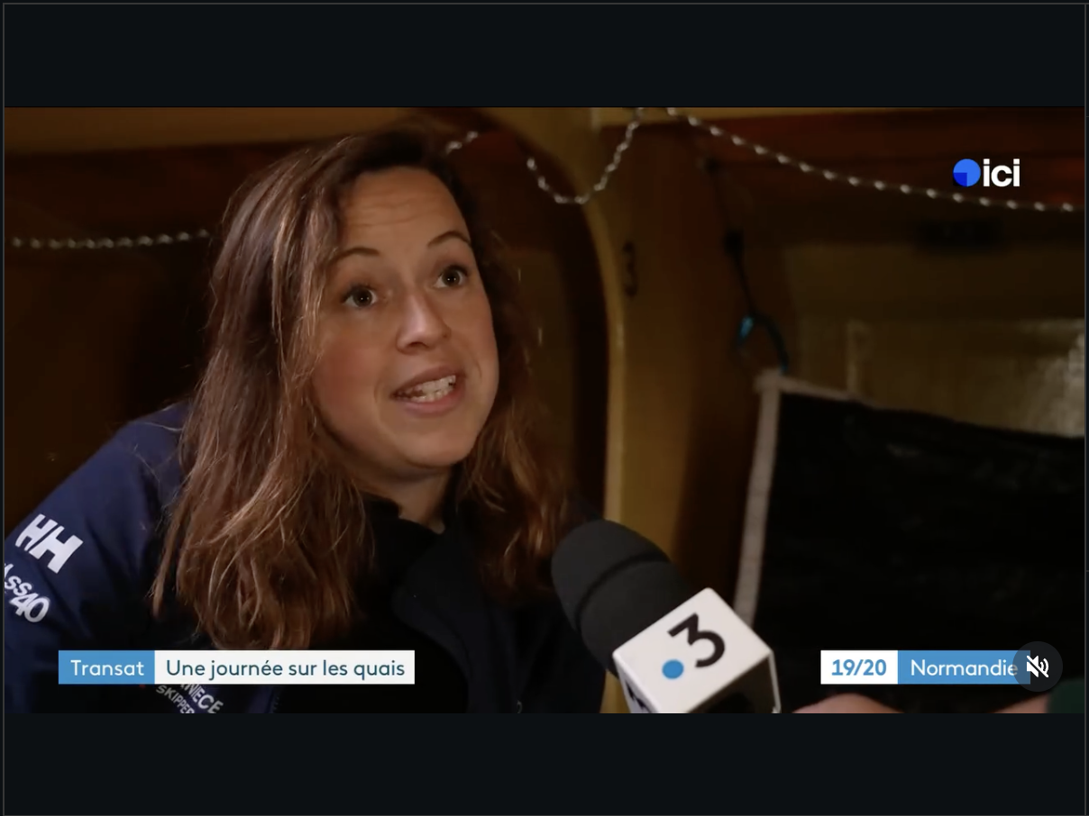Une femme parle à un micro lors d'une interview, dans un lieu en bois décoré avec des guirlandes lumineuses.