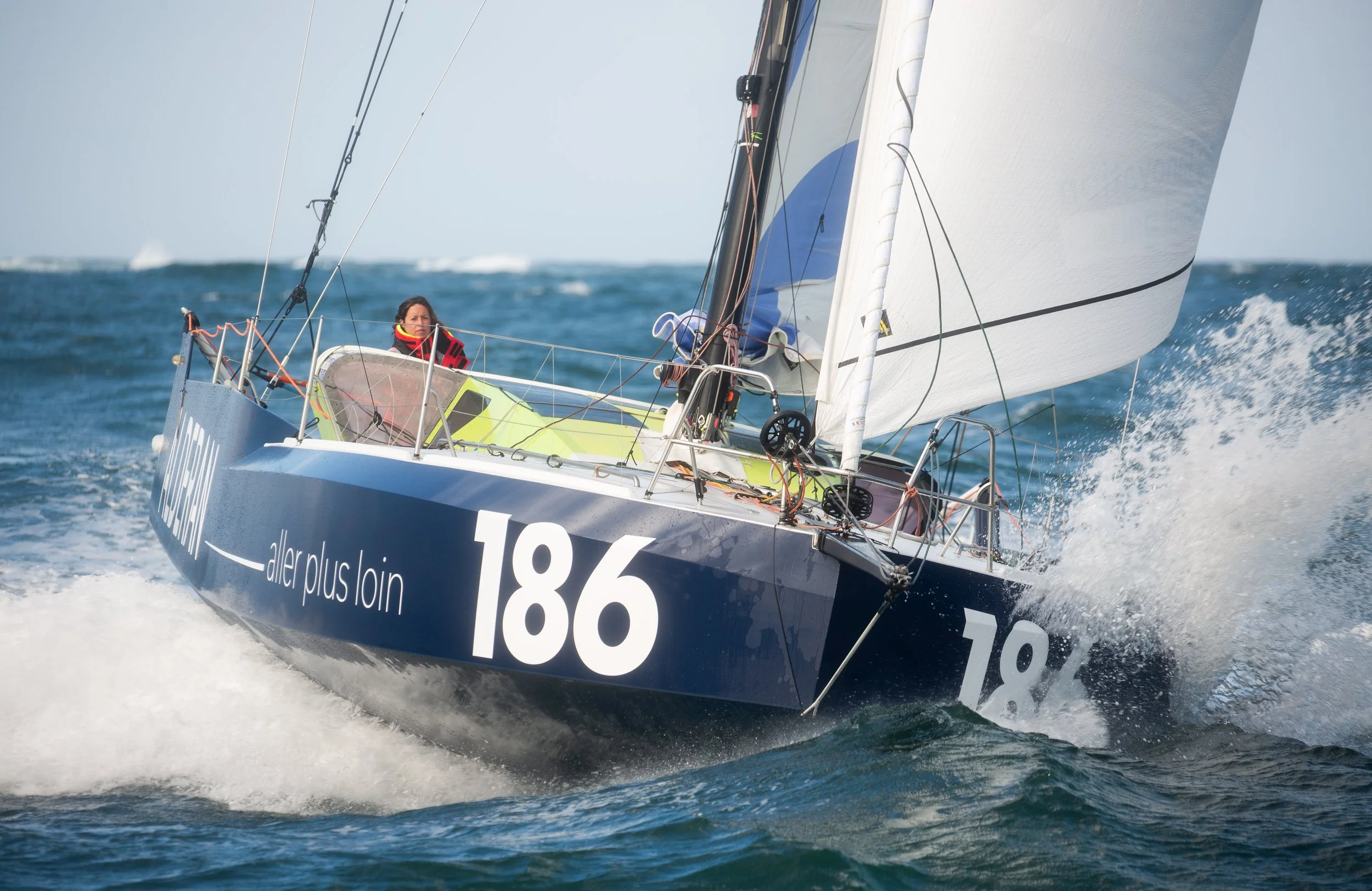 Un voilier naviguant à grande vitesse sur la mer avec une personne à bord, en arrière-plan un ciel clair.