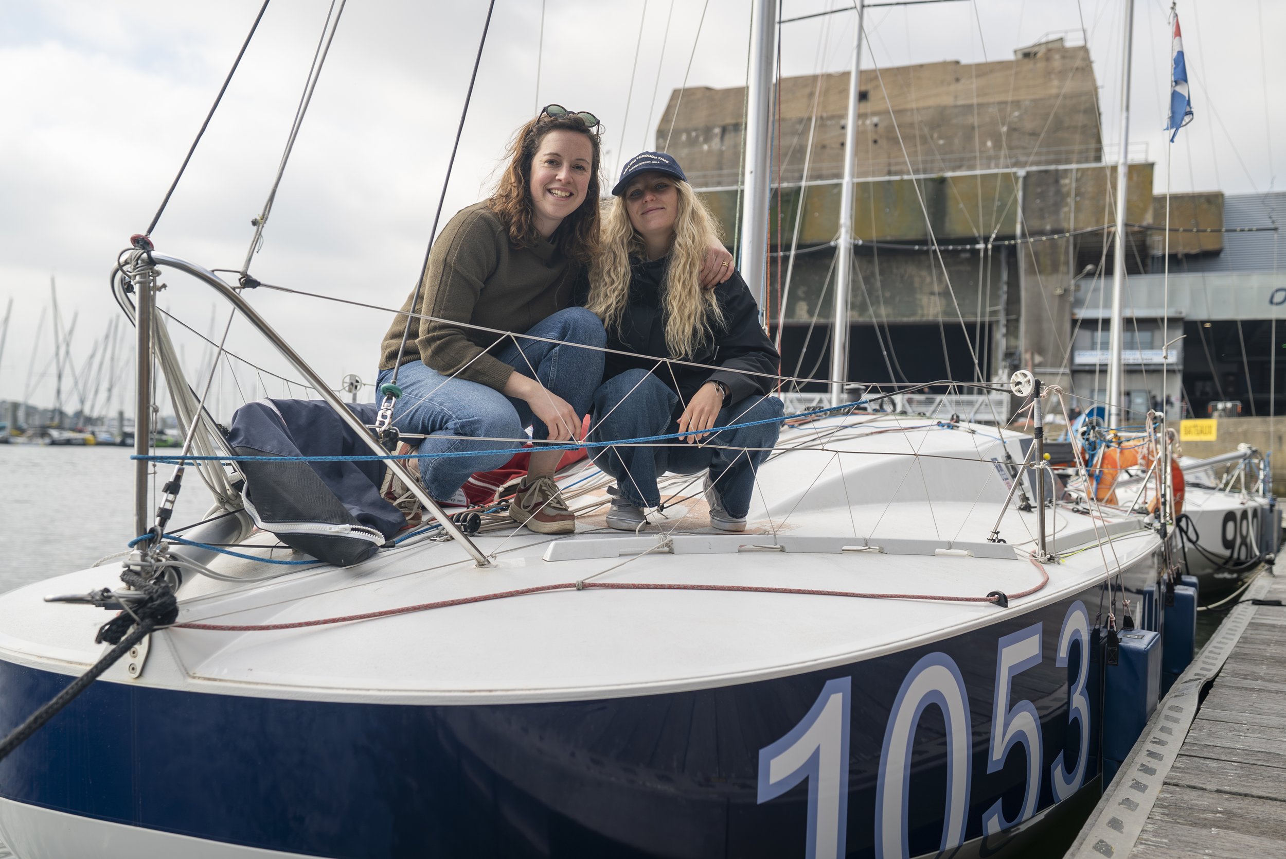 Deux jeunes femmes souriantes sur un bateau à quai, entourées de câbles et d'équipements de voile.