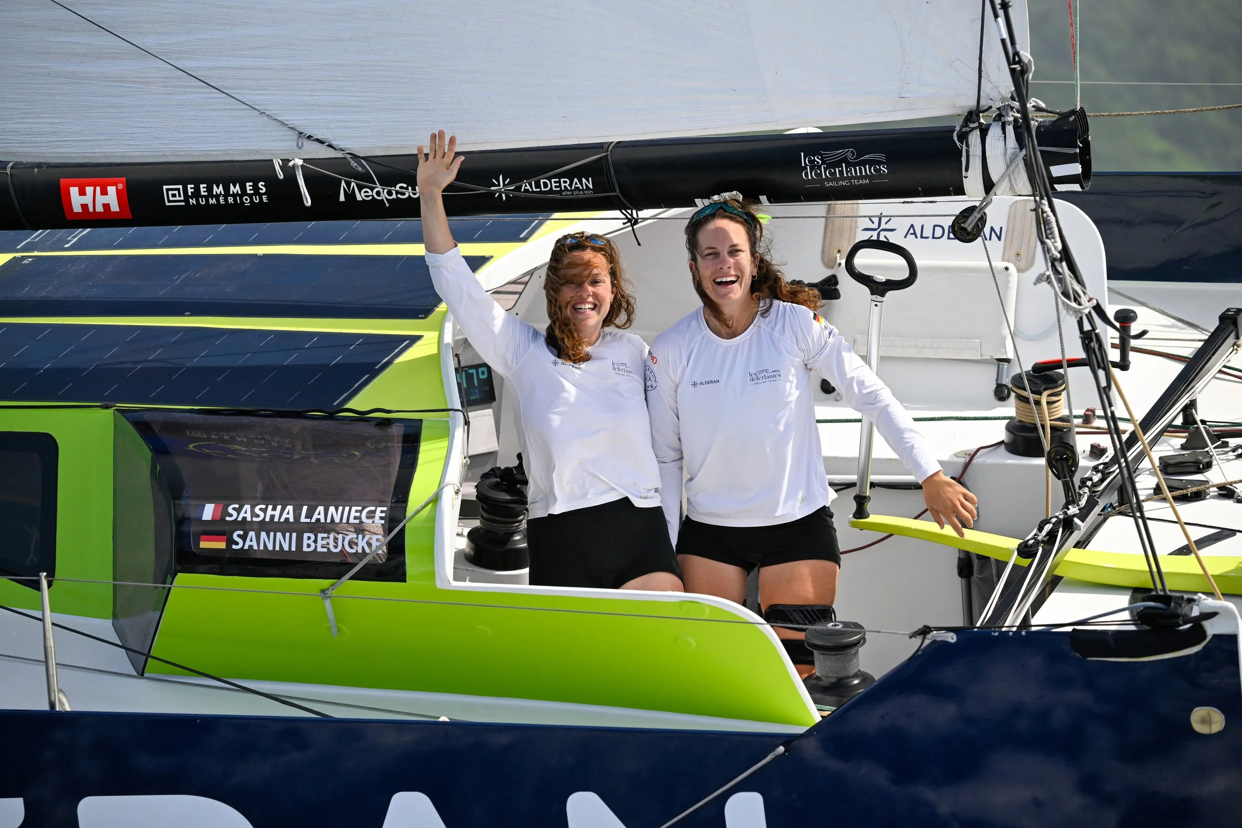 Deux femmes souriantes en vêtements blancs, assises dans un voilier, célébrant leur victoire ou leur participation à une compétition nautique.