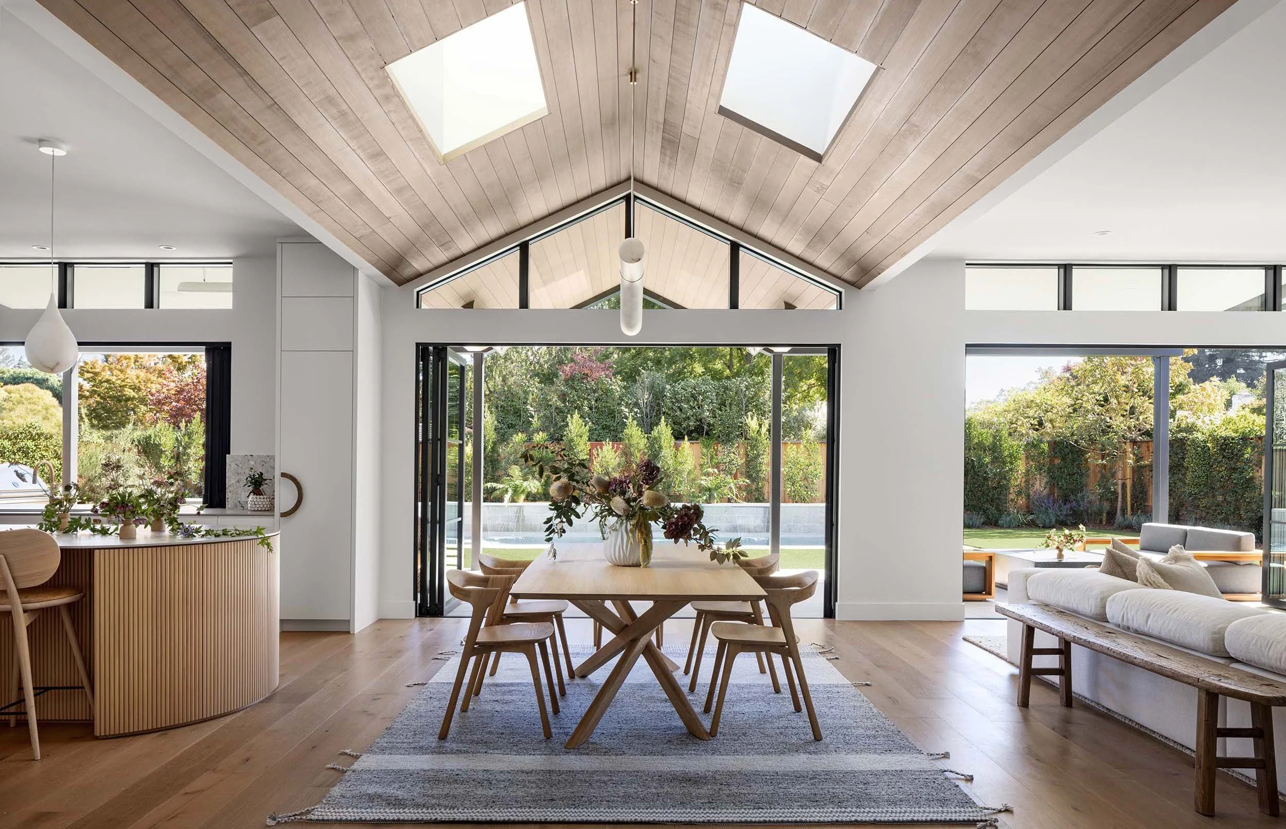 Modern California residential interior styled by Nicole Johnson Design featuring vaulted wood ceilings, skylights, and indoor outdoor dining space