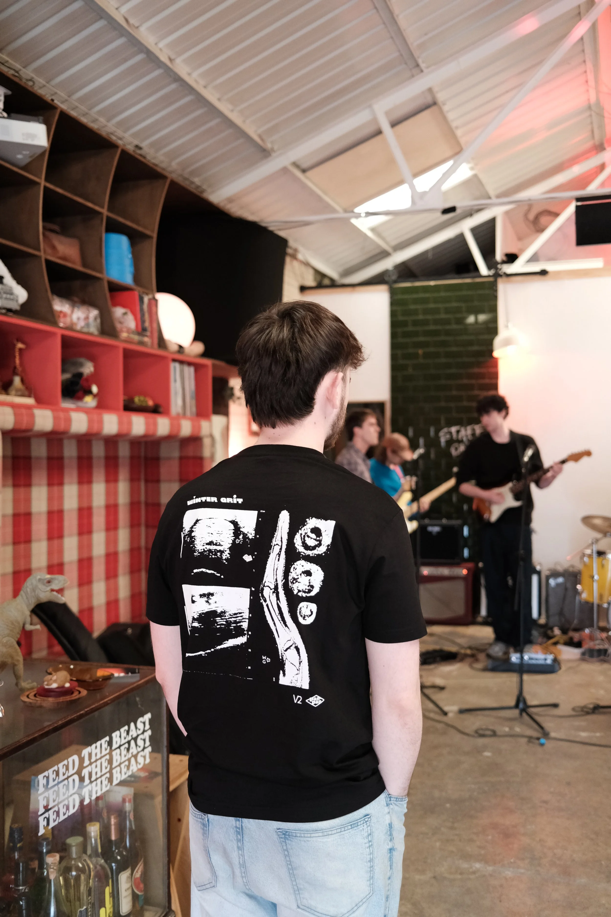 Person wearing the Winter Grit Rest Day Volume 2 graphic T-shirt at an indoor community event with live music.