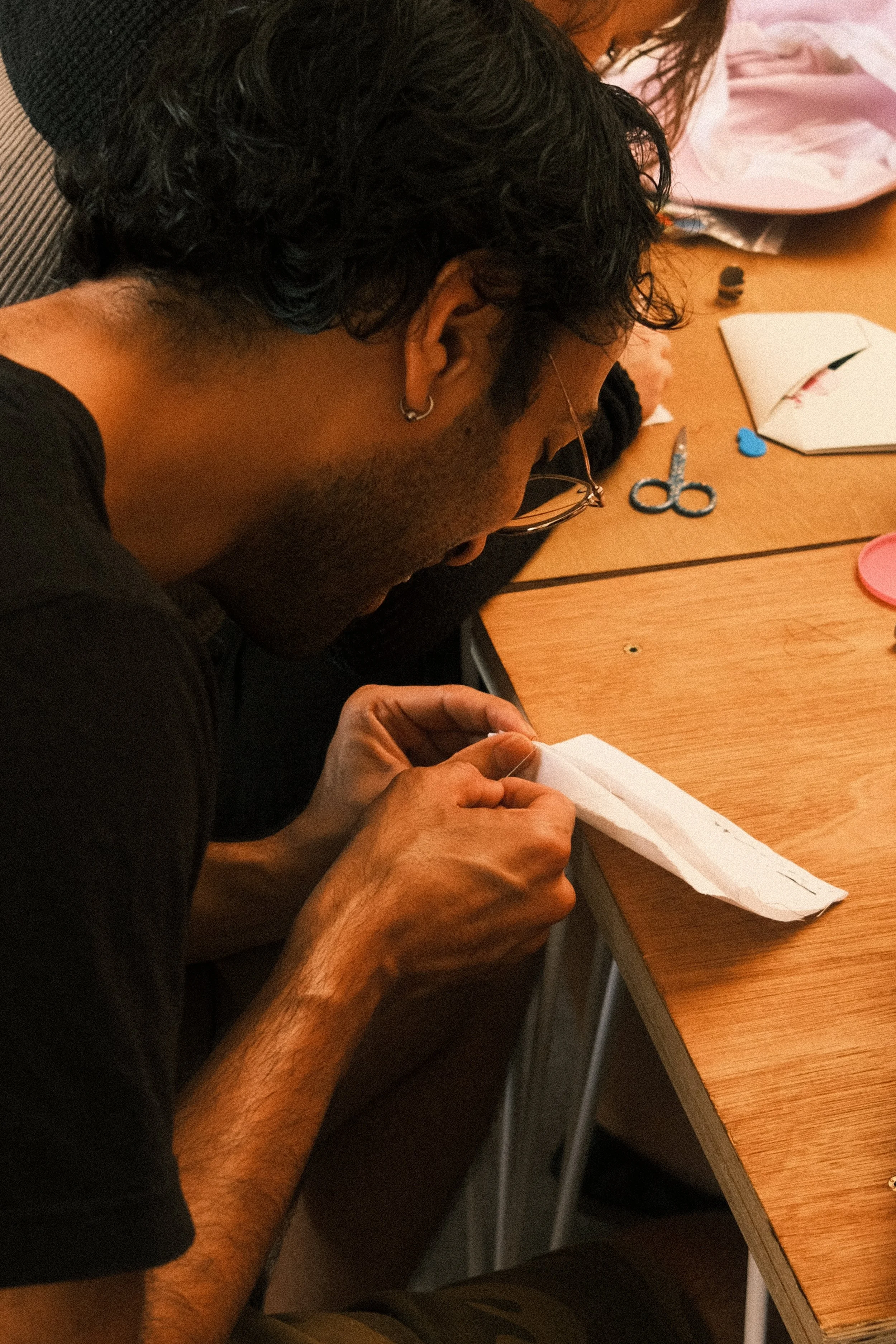 Person working by hand on a craft project with scissors, paper and materials spread across a table.