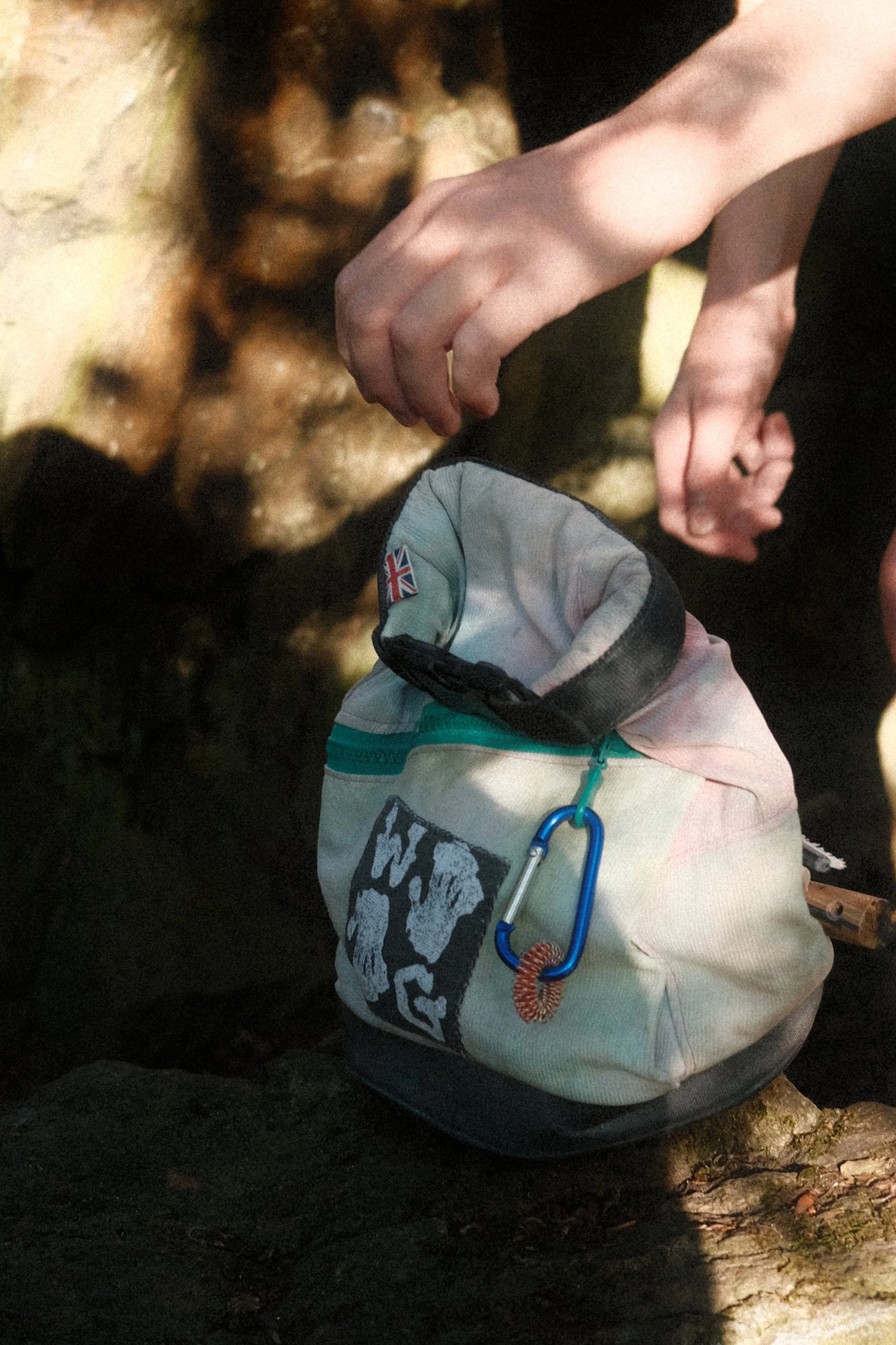 Close-up of a climber carrying a carabiner and chalkbag at an outdoor bouldering area.