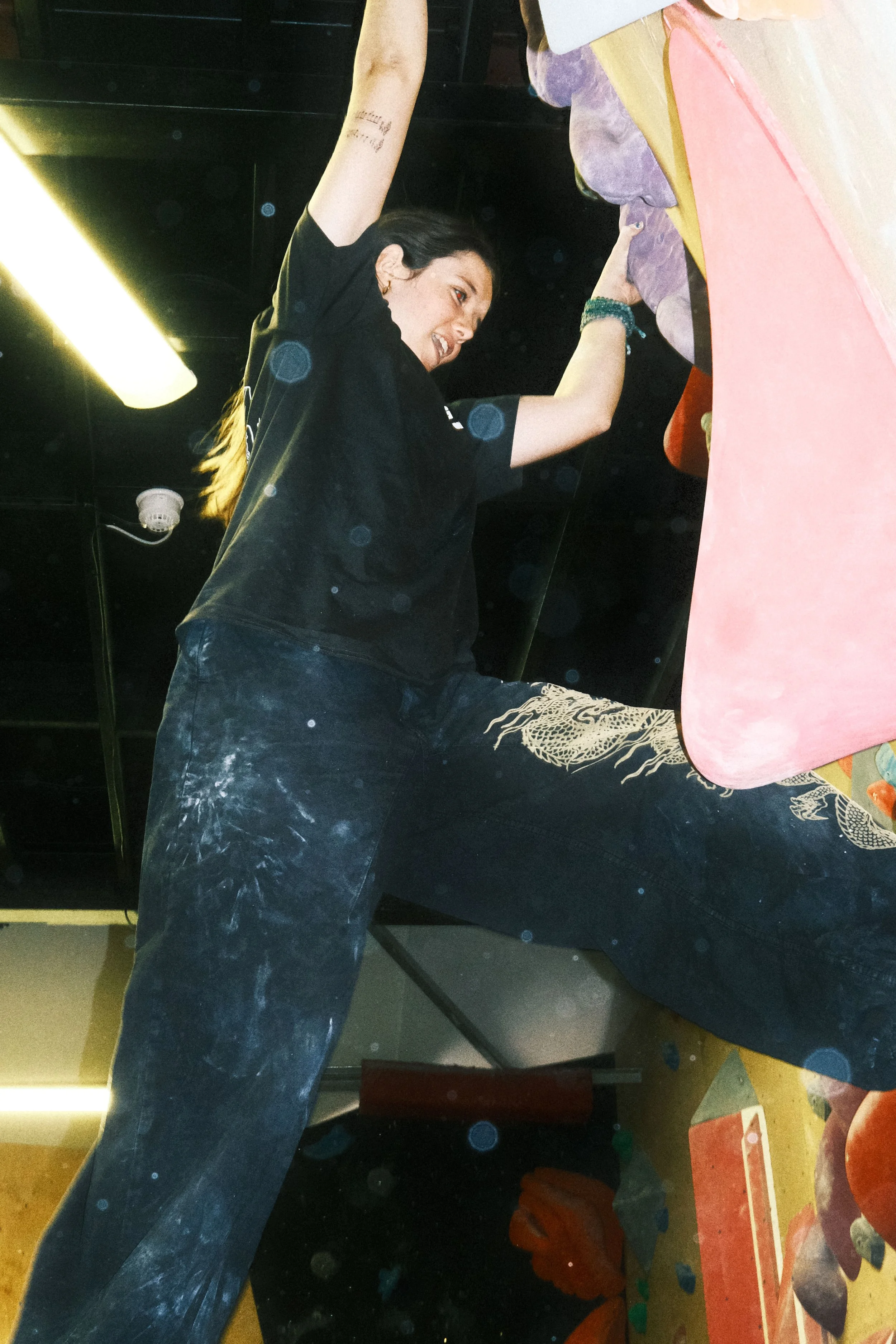 Climber in a black Winter Grit x Climbing Co T-shirt attempting an overhanging indoor bouldering route.