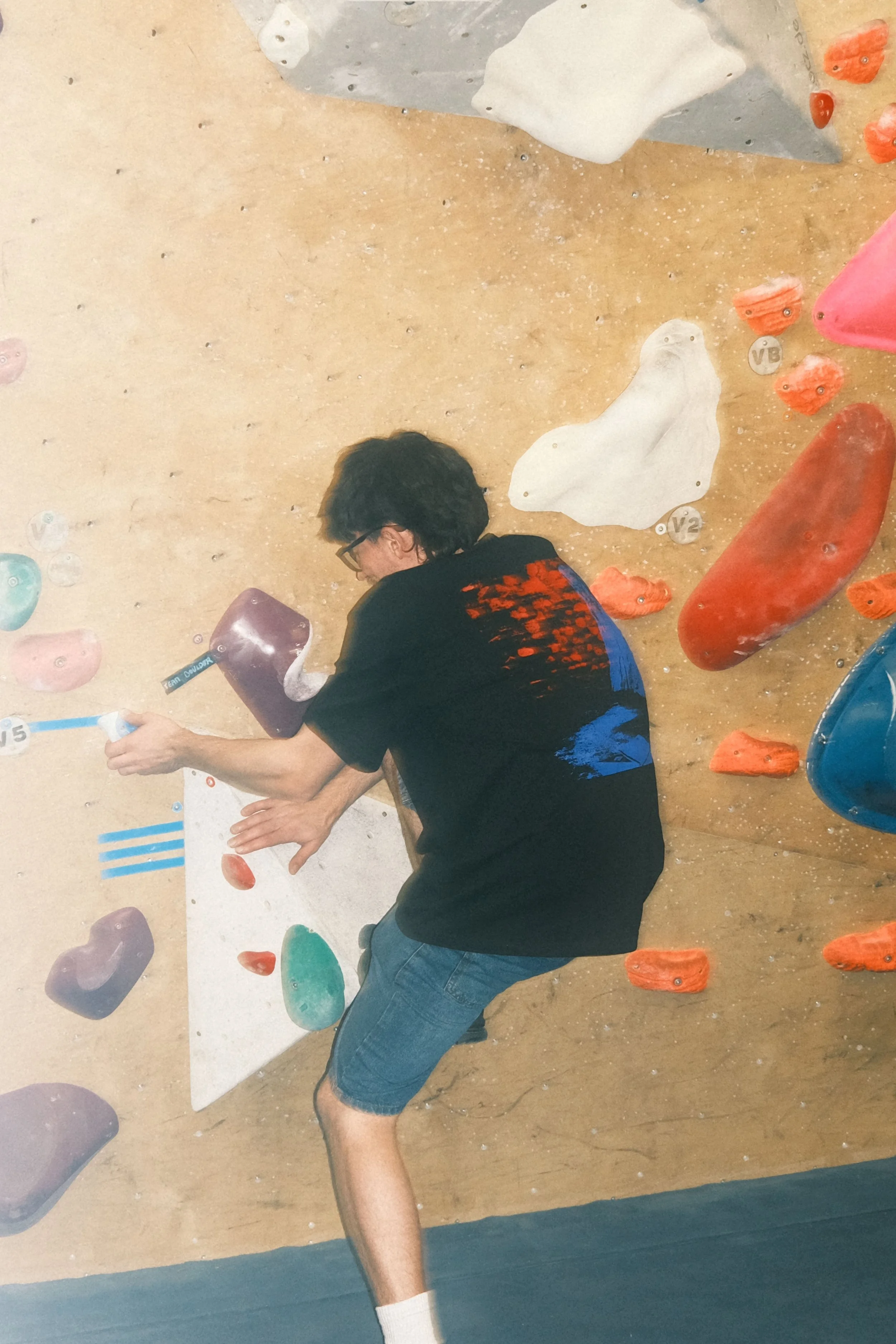 Climber wearing the Winter Grit x MADE Contact Point black oversized T-shirt while reaching across colourful indoor bouldering holds.