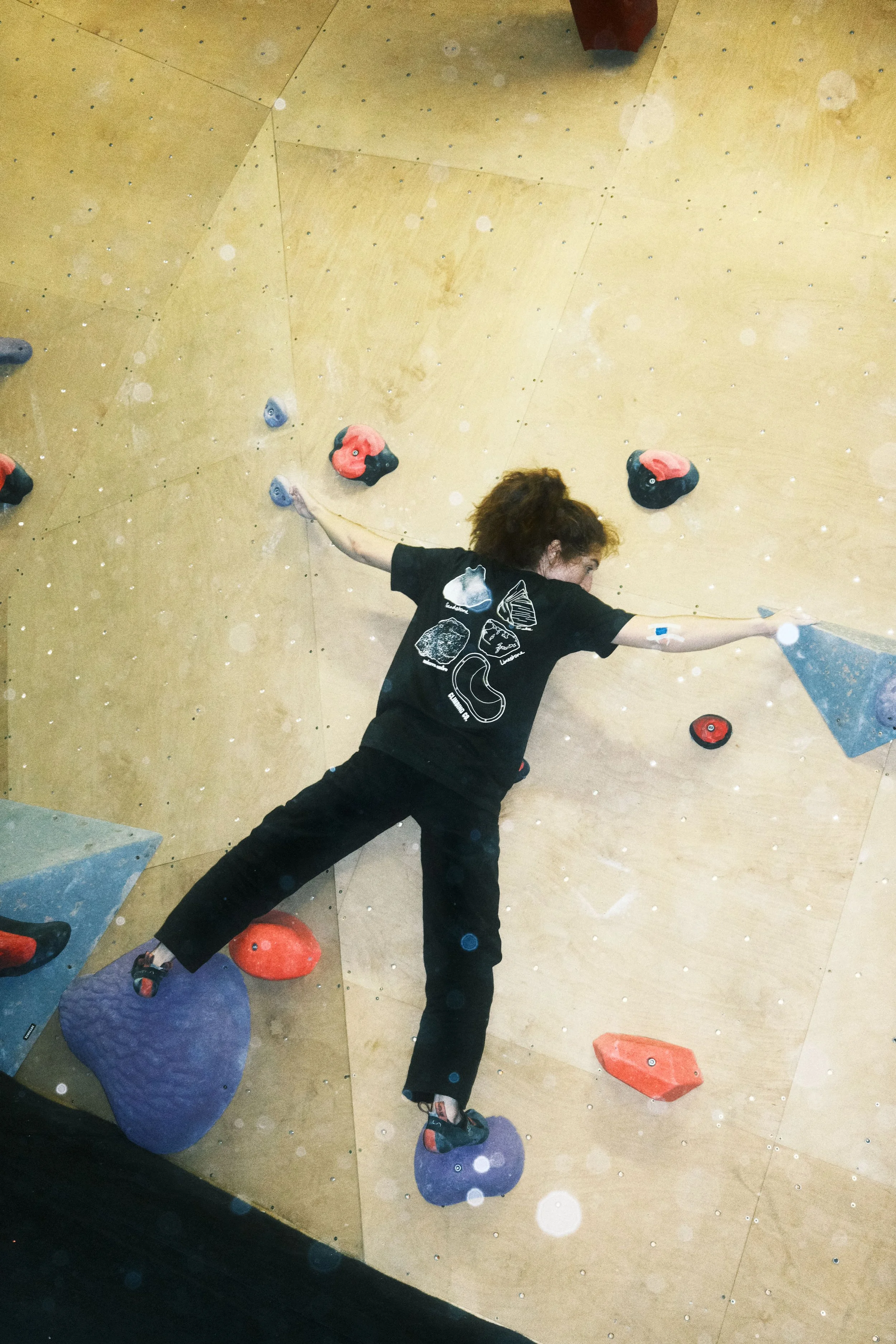 Rear view of a climber wearing the Winter Grit x Climbing Co Rock Textures Tee on a colourful indoor bouldering wall.