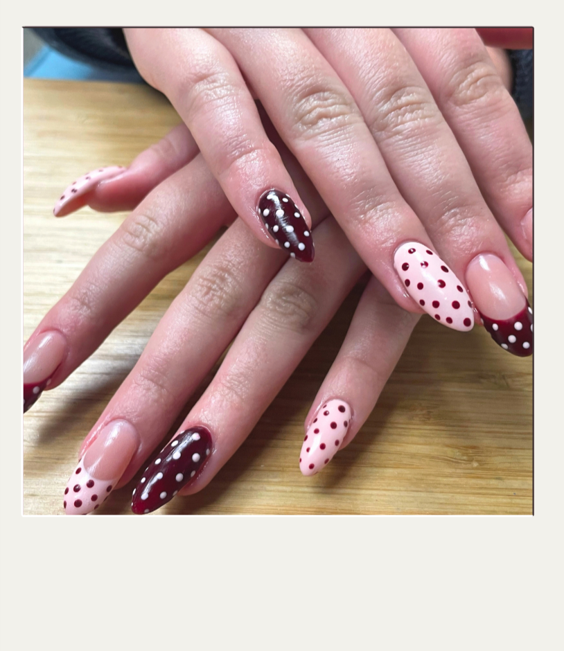Close-up of hands with manicured nails featuring polka dot designs in white, red, and dark brown colors.