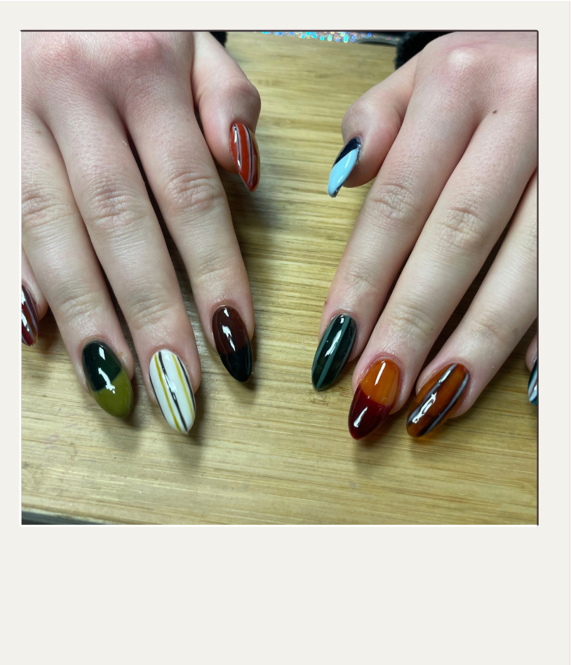 Manicured fingernails with multicolored nail polish in various designs on a wooden table.