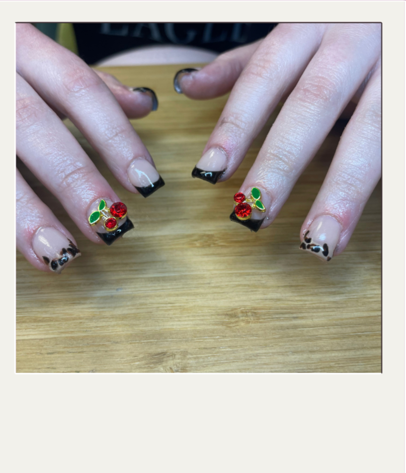 Nail art on natural nails featuring a leopard print design on the thumbs and pinky fingers, and cherry-themed decorations with red rhinestones and green leaves on the middle fingers.