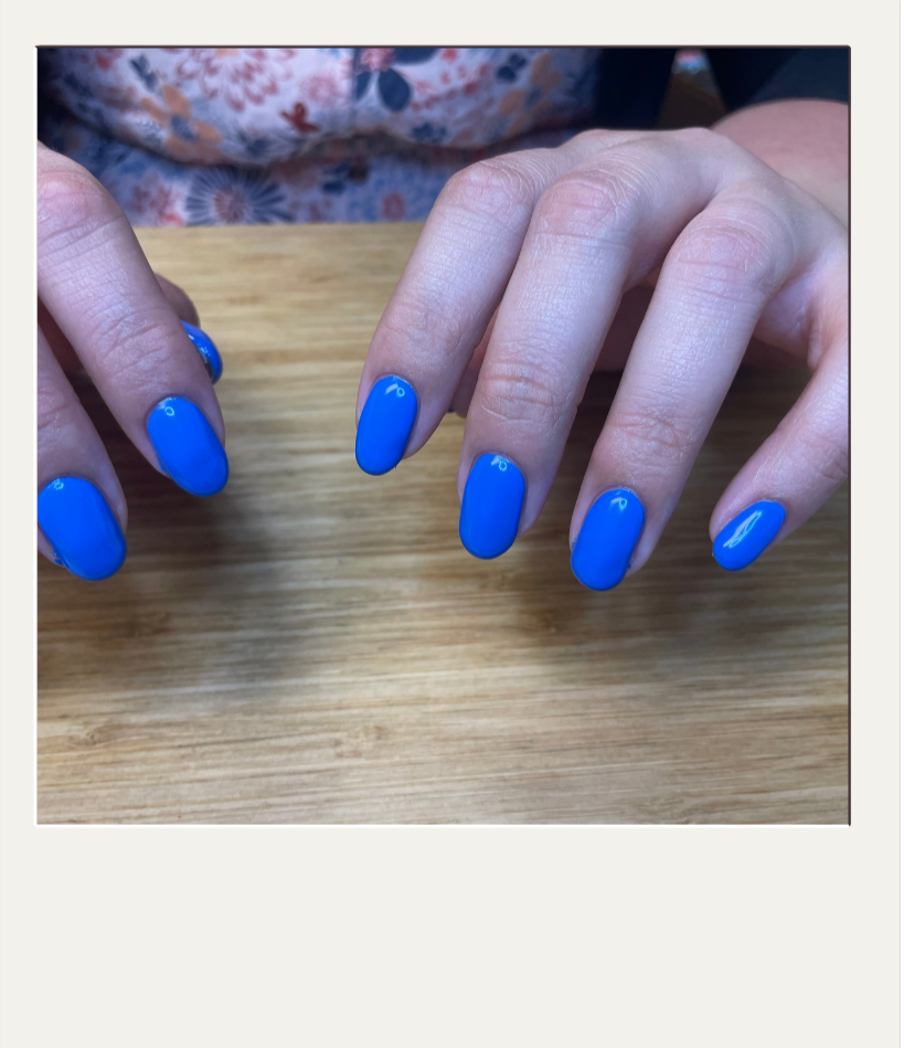Close-up of hands with bright blue painted nails resting on a wooden surface.