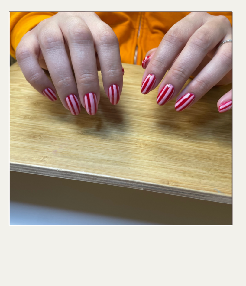 Close-up of a person's hands with red and white striped nail polish resting on a wooden surface, with part of an orange jacket visible in the background.