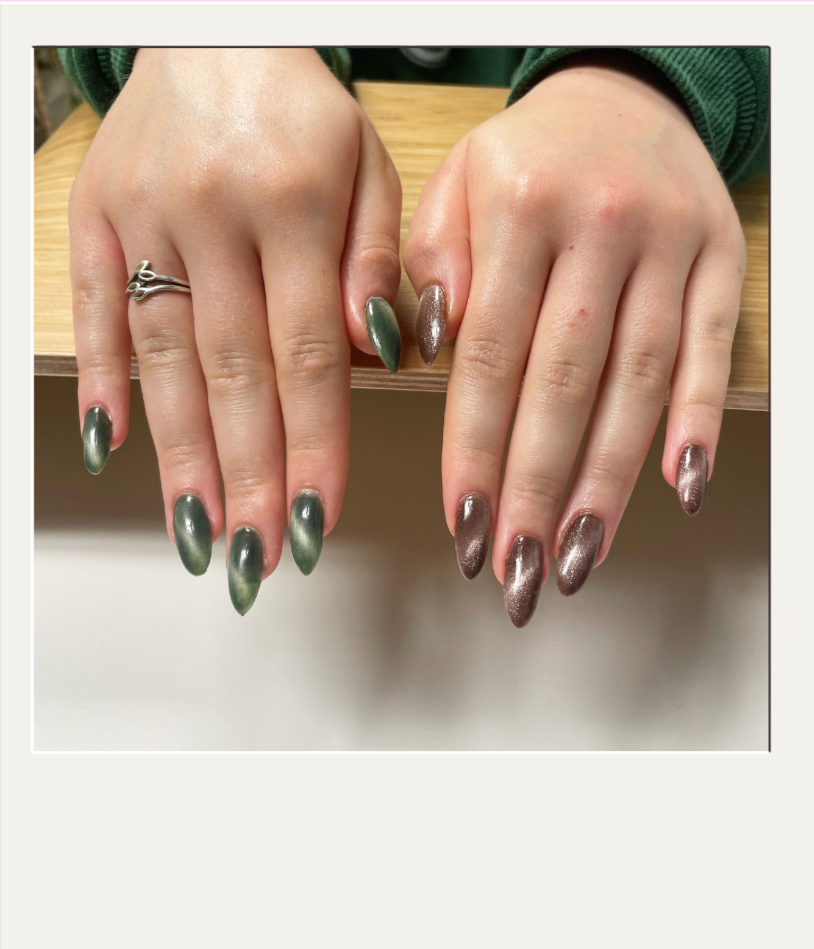 Hands with metallic green and bronze-colored nail polish resting on a wooden surface.