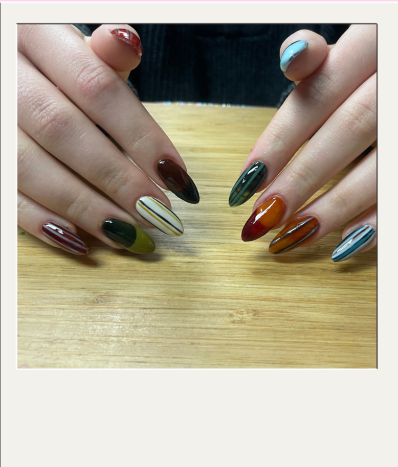 Close-up of two hands with colorful, patterned, and striped nail art, resting on a wooden surface.