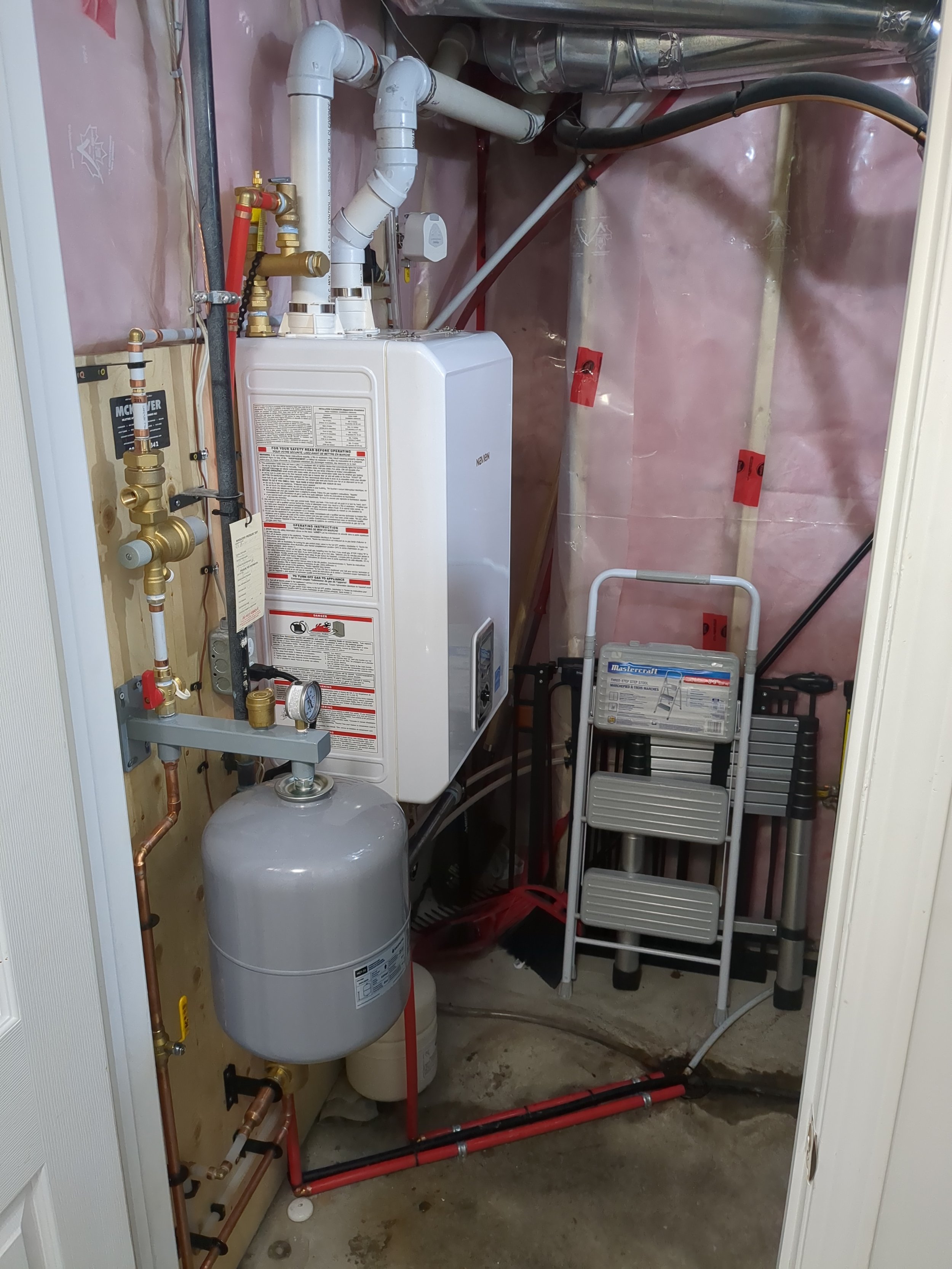 A utility closet with a boiler, plumbing pipes, and a step ladder.