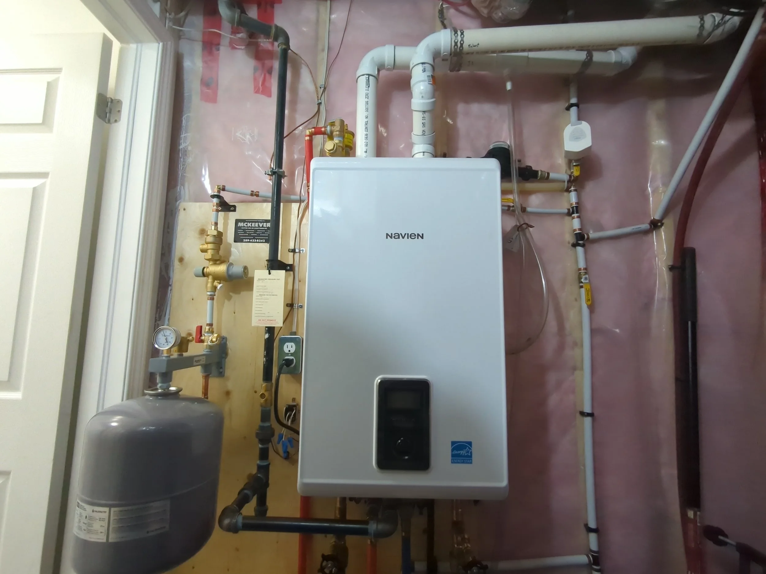 Installation of a Navien tankless water heater in a utility room with exposed plumbing and electrical connections.