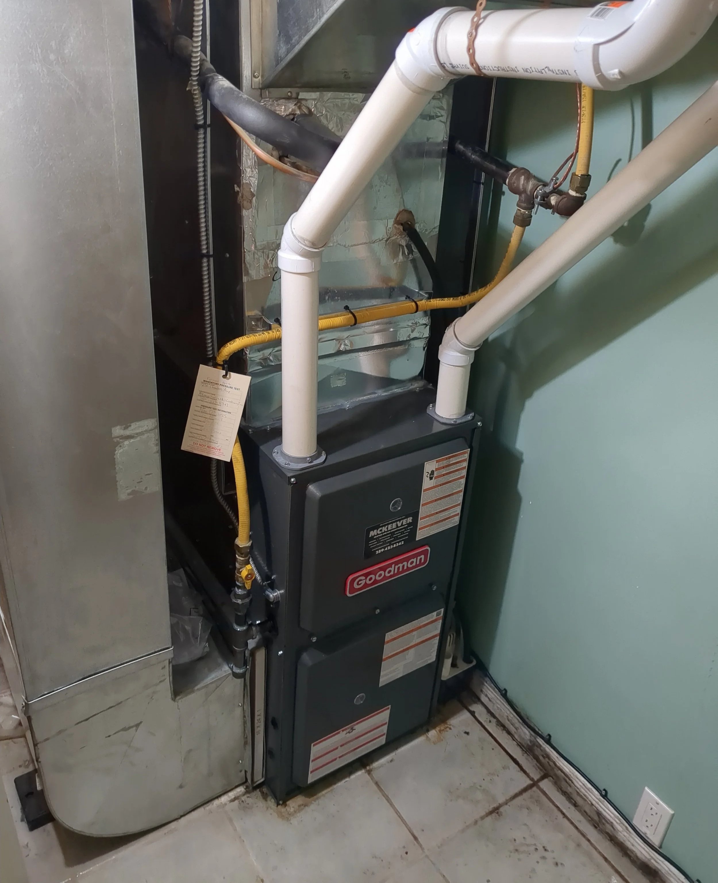 A Goodman furnace with pipes and ducts in a utility room.