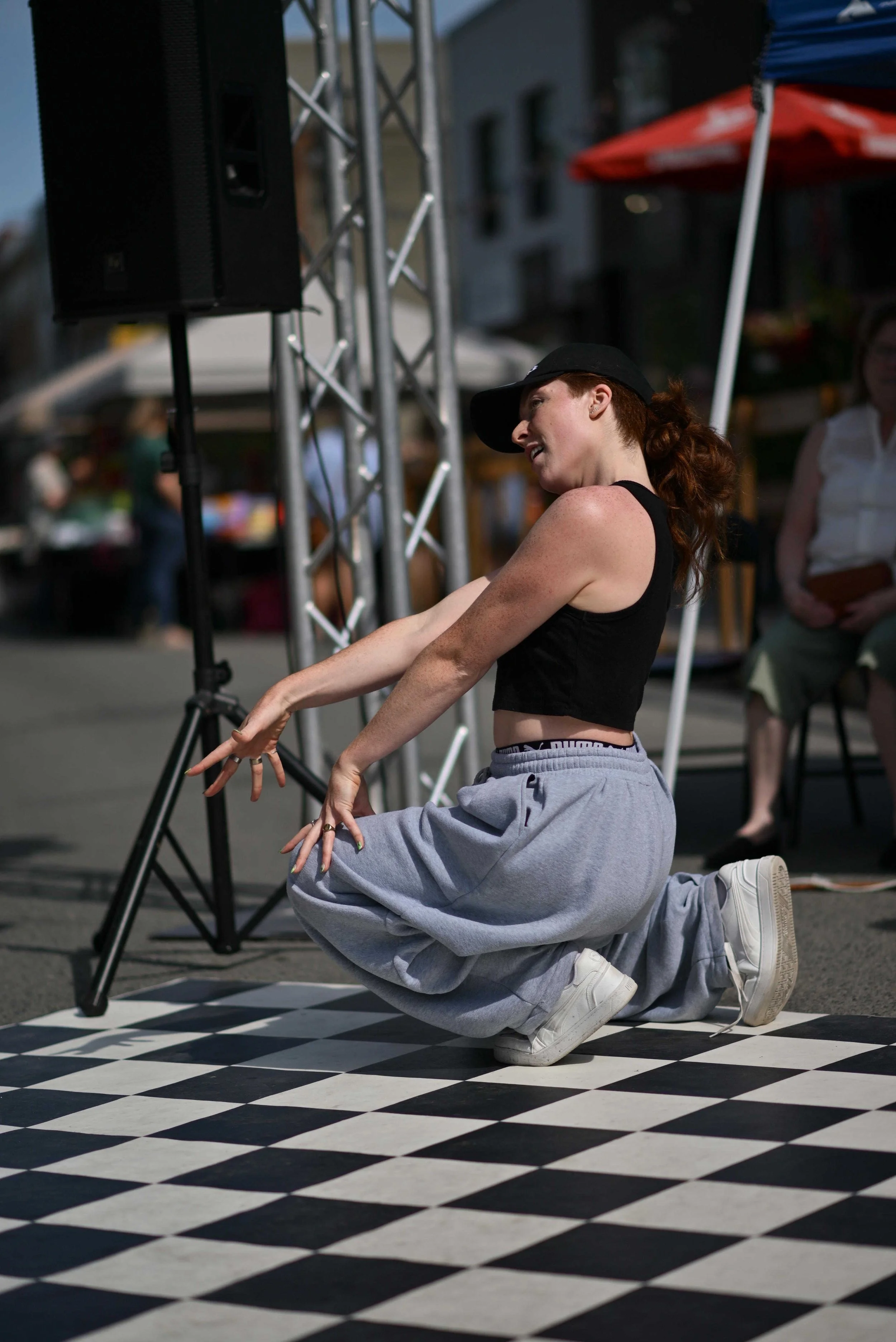 Groupe de jeunes femmes posant sur un échiquier géant avec un DJ en arrière-plan lors d'un événement en plein air au coucher du soleil.