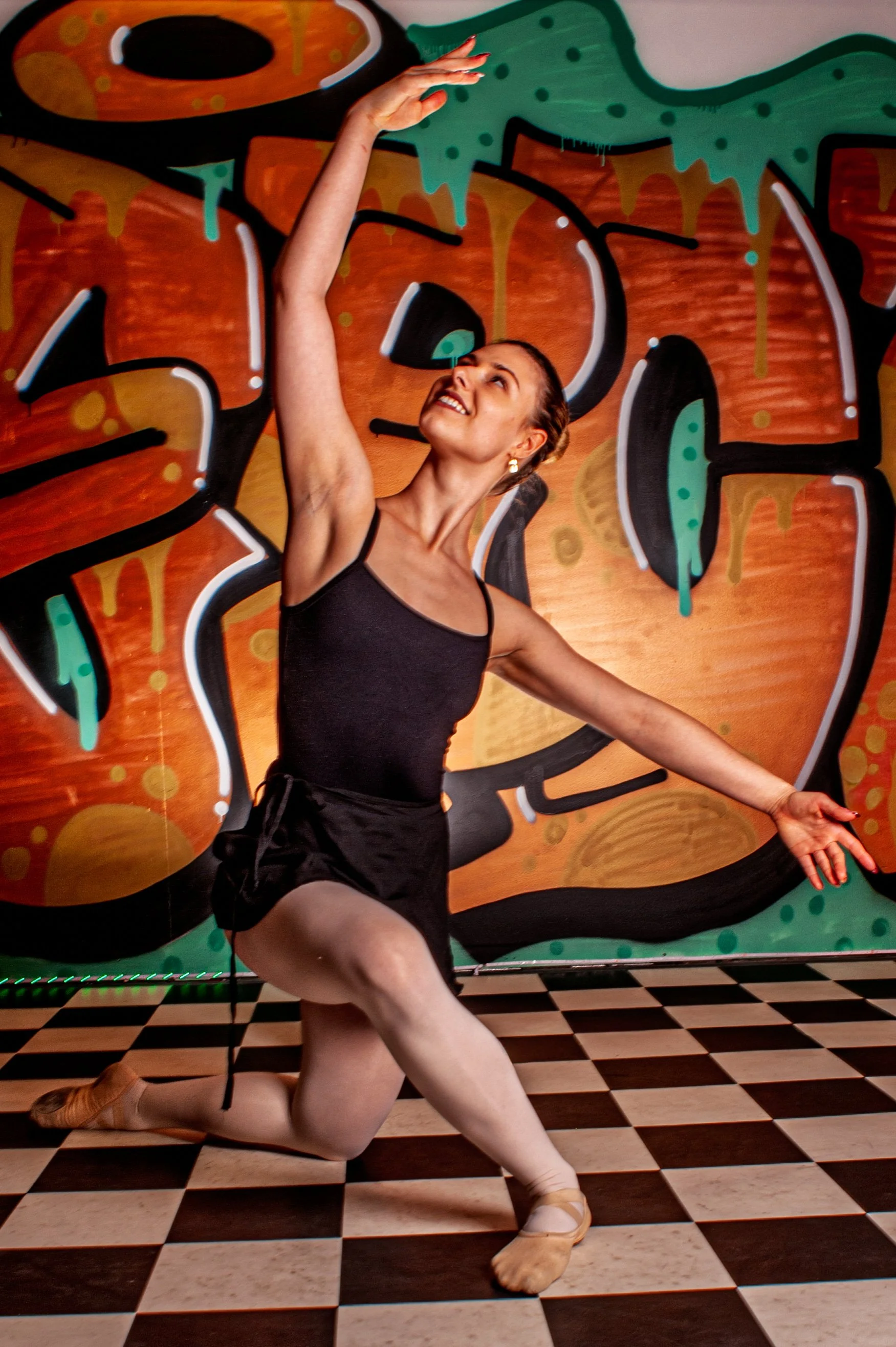 Femme en tenue de danse ballet, posant sur un sol à damier, devant un mur coloré avec graffiti