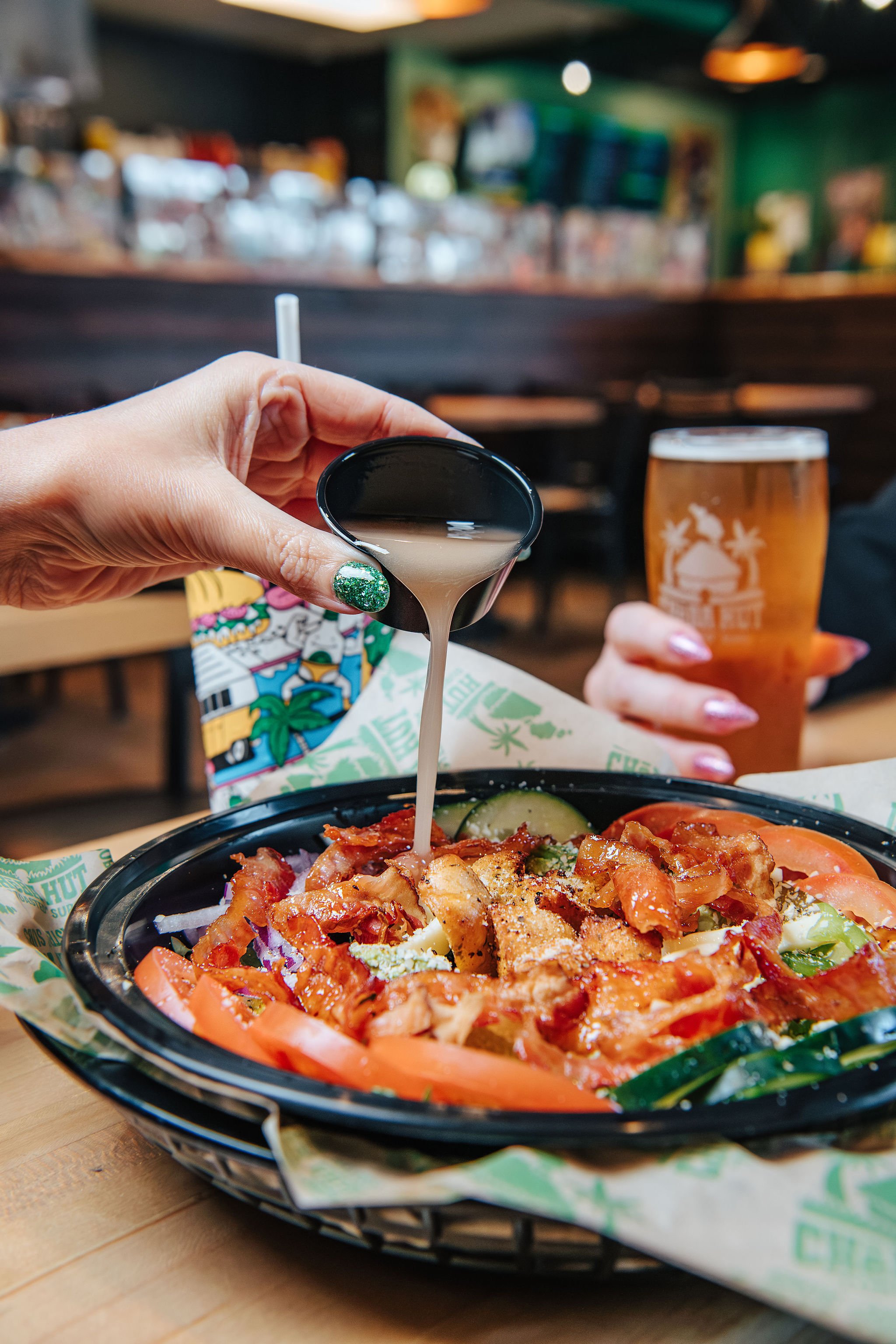 Pouring creamy dressing or sauce onto a taco salad with vegetables and meat at a restaurant.