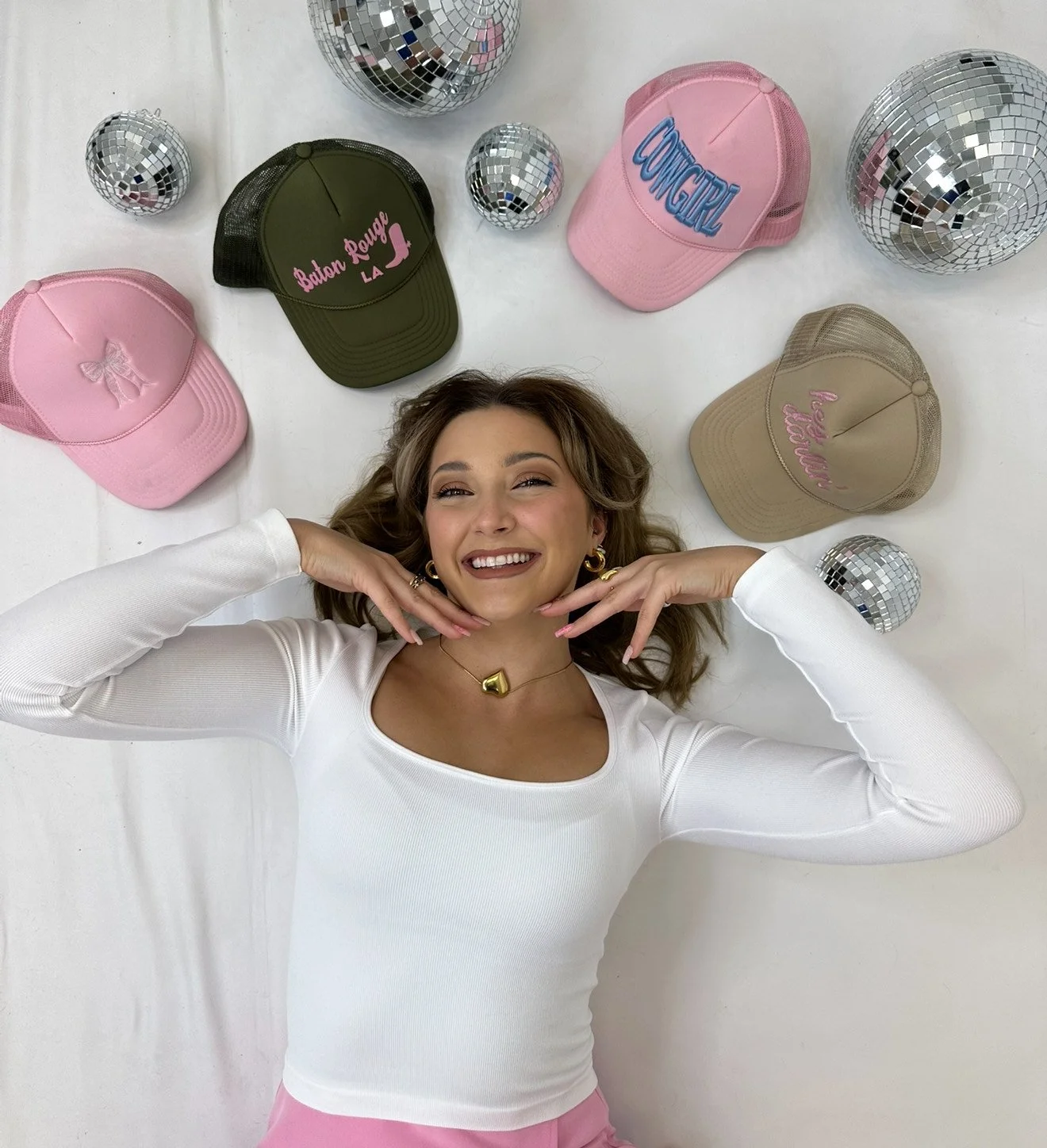 A blond woman laying down surrounded by hats and disco balls