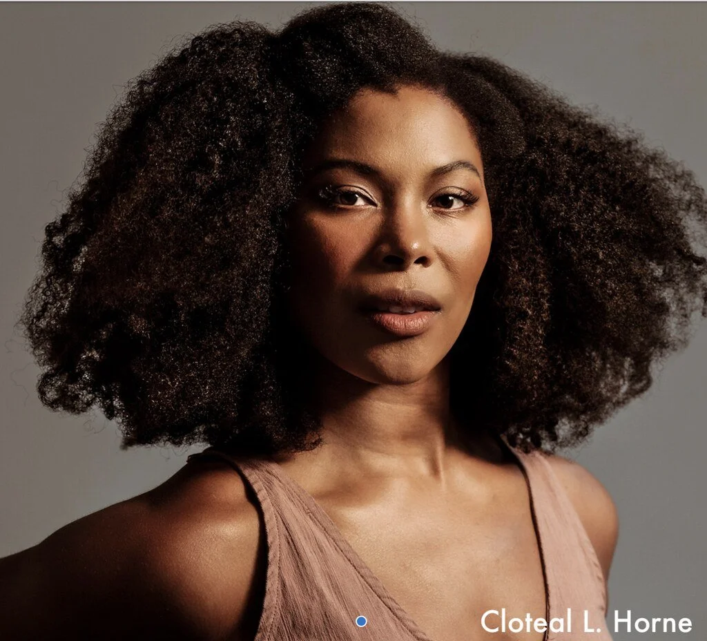 Close-up portrait of a woman with short black hair, smiling subtly, wearing pearl earrings and a pink top.