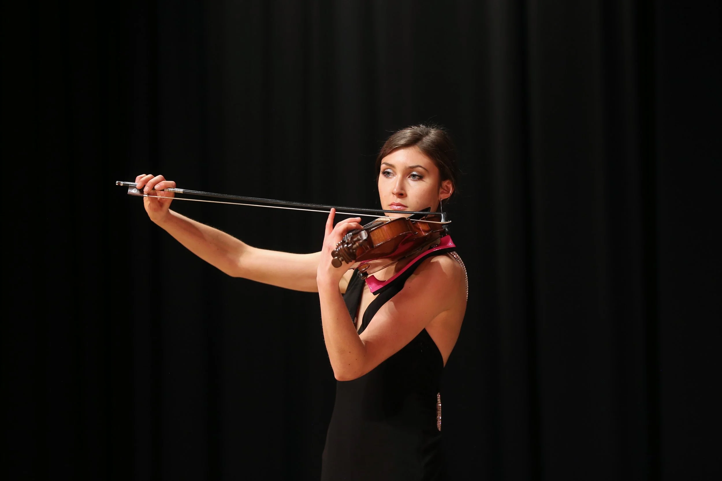 Young woman playing the violin on stage against a black curtain.