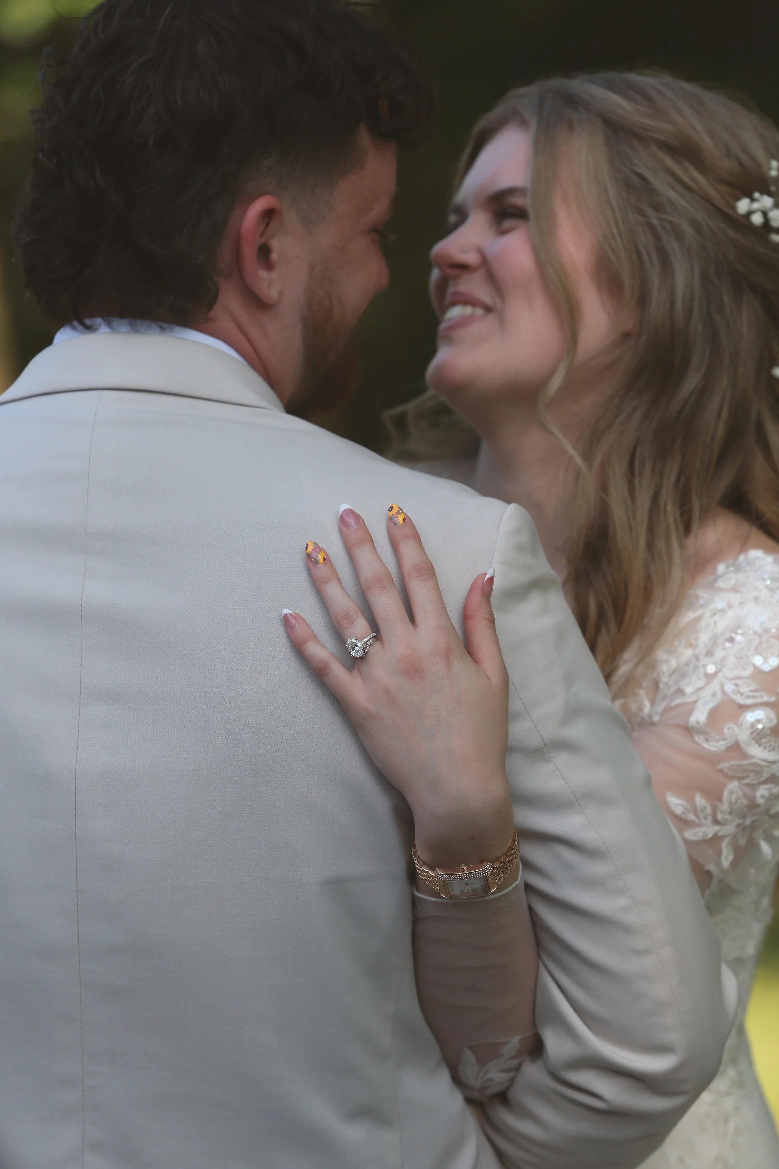 A close-up of a couple embracing on their wedding day with the bride's hand on the groom's shoulder, showing her wedding ring and manicure.