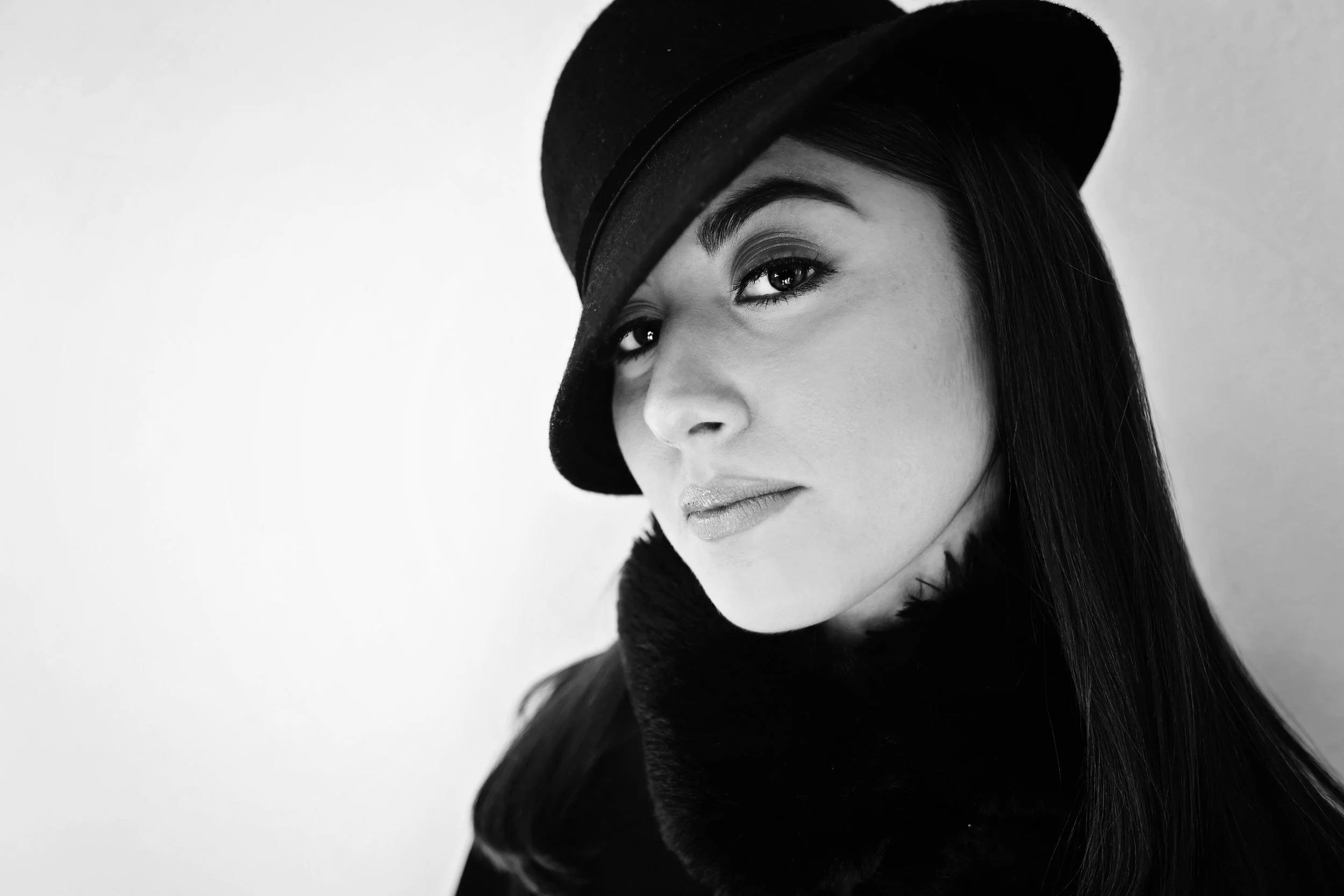 Black and white portrait of a woman wearing a hat and a scarf, looking at the camera with a slight smile.