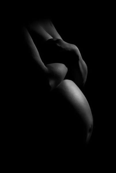 A black and white photo of a person's back and side, with the arms wrapped around the body, highlighting the curve of the shoulder and waist.