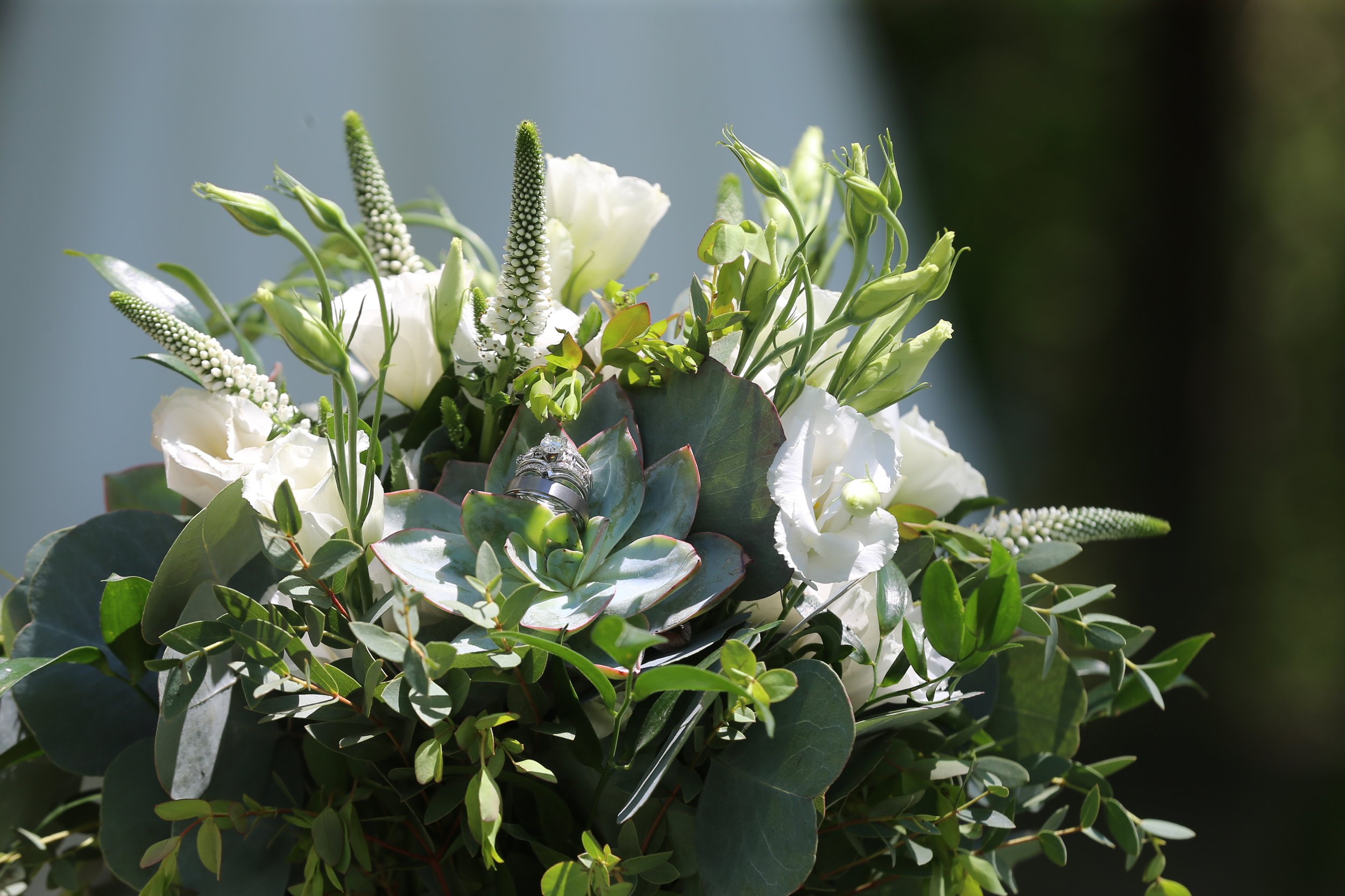 A floral arrangement of white flowers and greenery with wedding rings placed in the center.