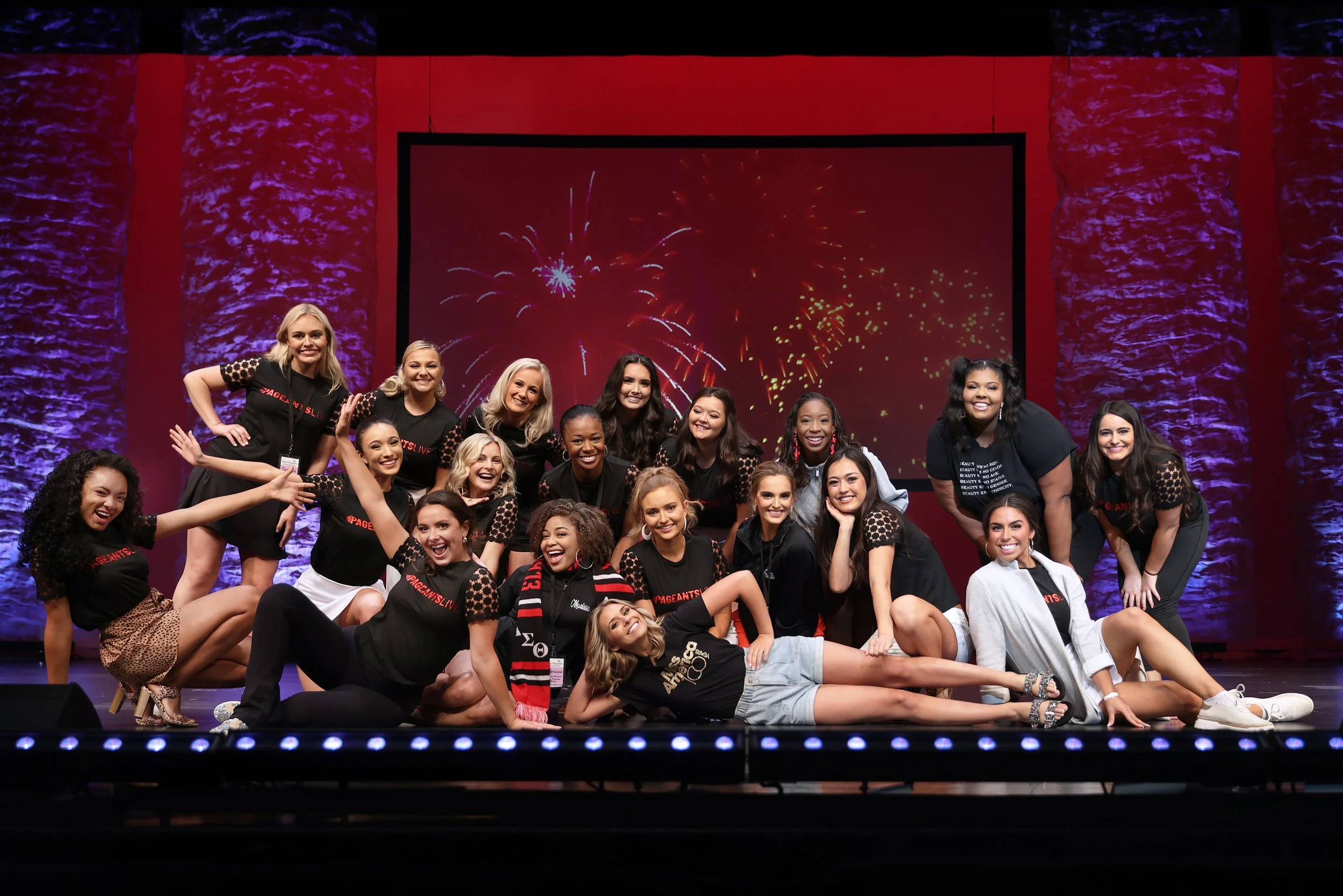 Group of women on a stage celebrating, with fireworks displayed on a screen behind them.