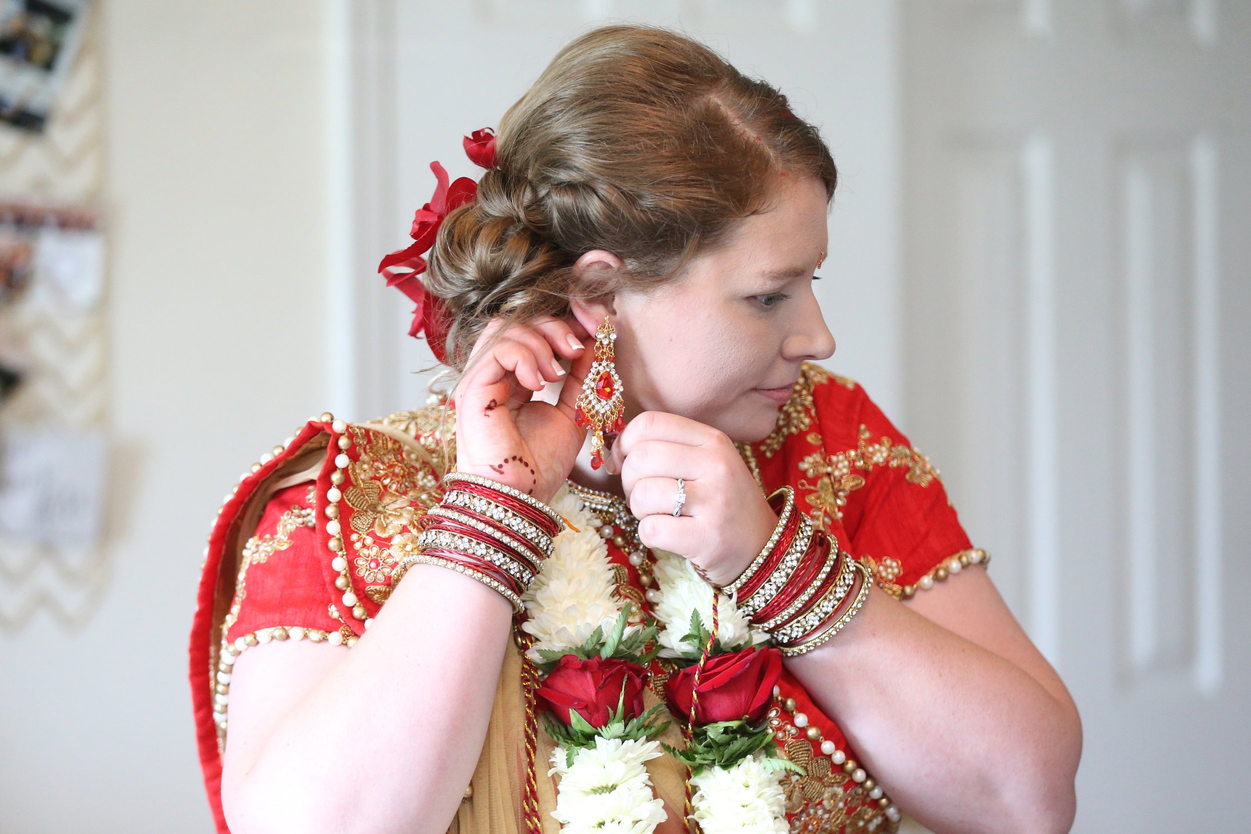 A woman dressed in traditional South Asian bridal attire adjusting her earrings.