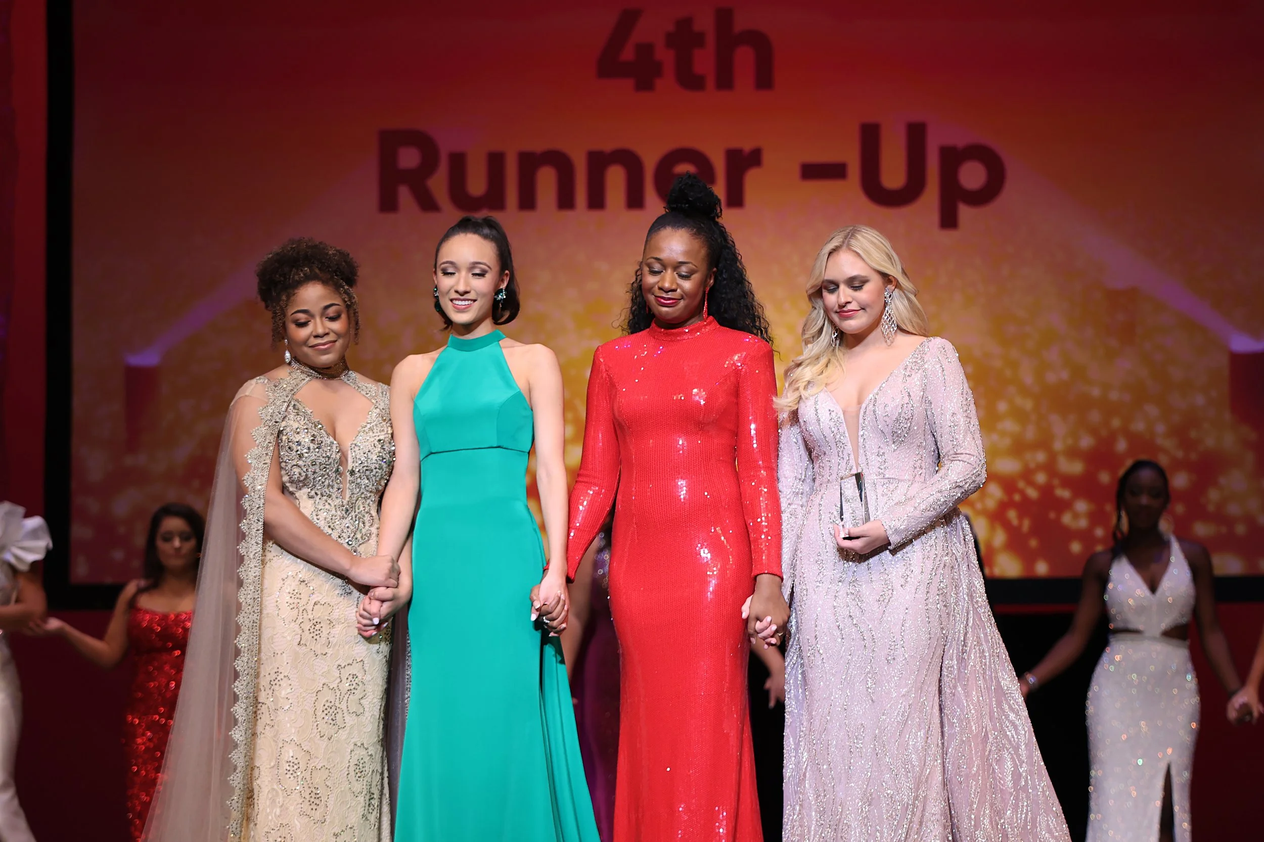 Award ceremony with five women in evening gowns on stage. A large screen behind them displays '4th Runner-Up'. The women appear to be finalists in a beauty or talent contest.