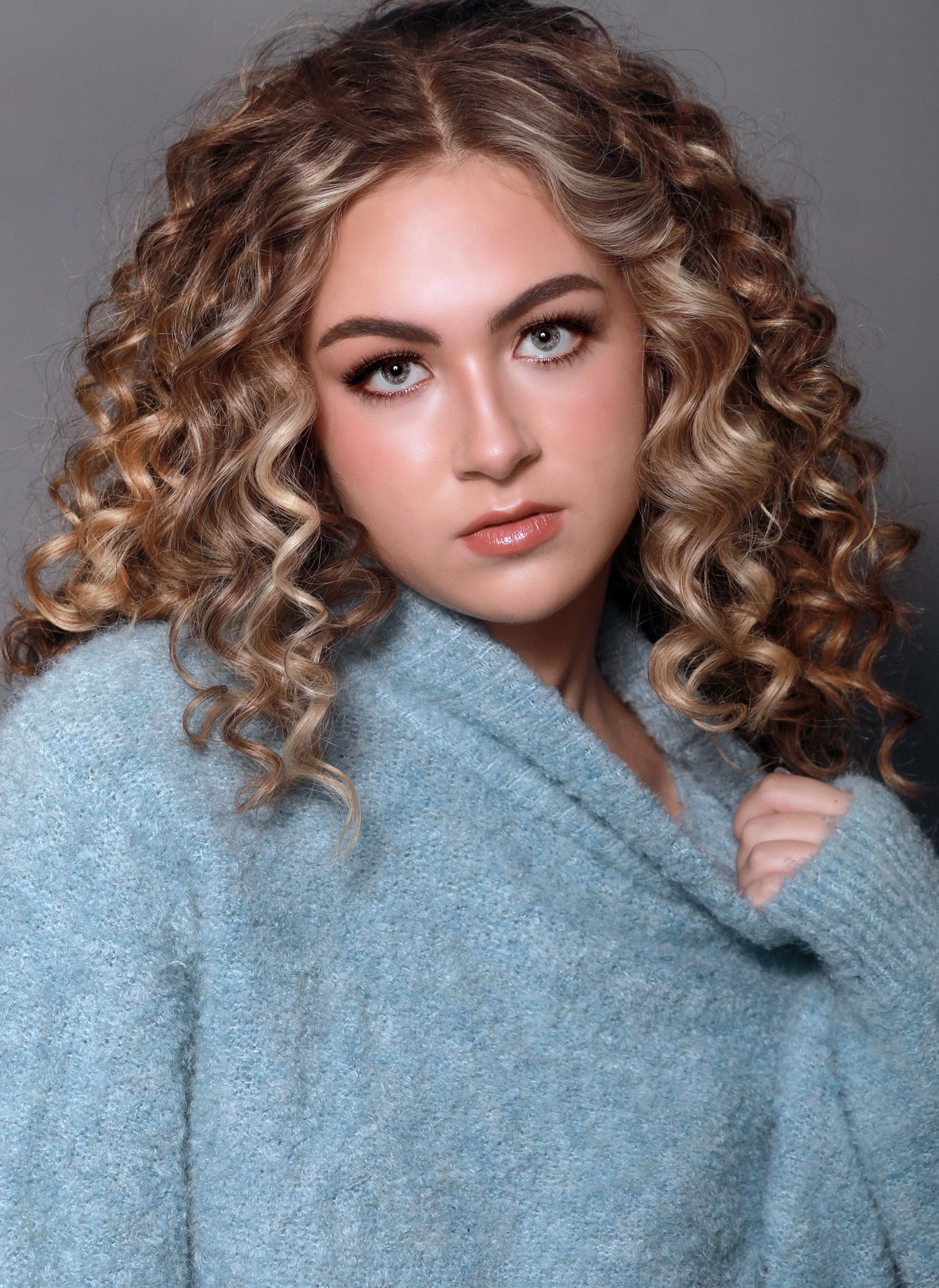 A young woman with curly blonde hair wearing a gray sweater.