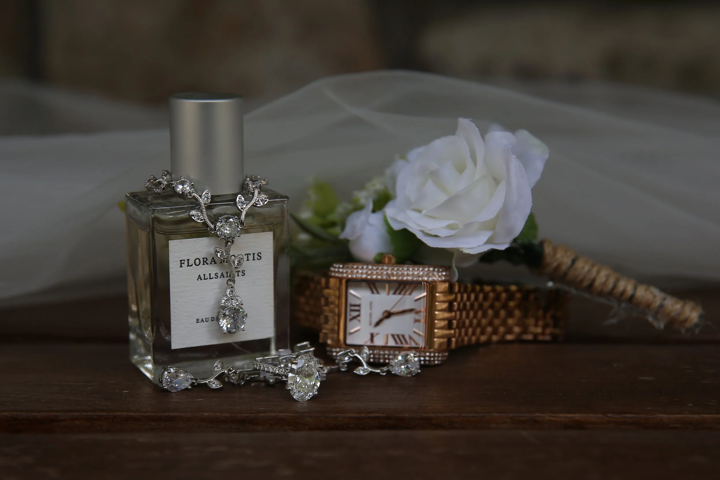 Jewelry, white flower, and a watch on a wooden surface with a white background.