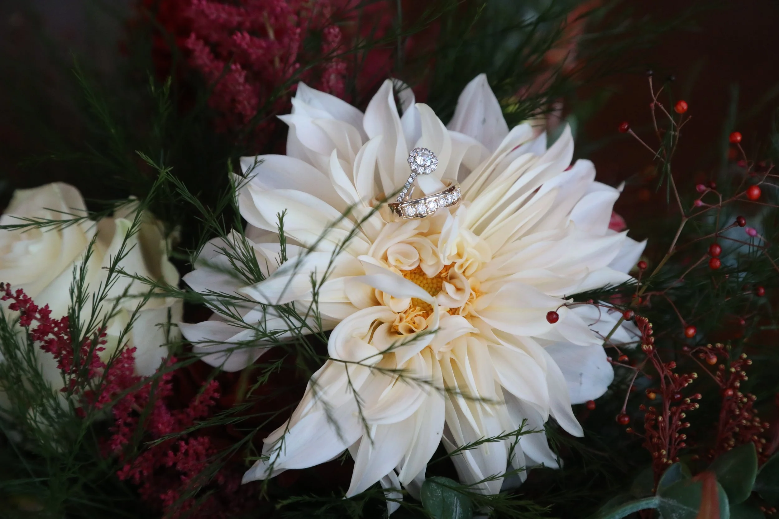Wedding rings placed on a white flower in a bouquet, surrounded by various flowers and greenery.
