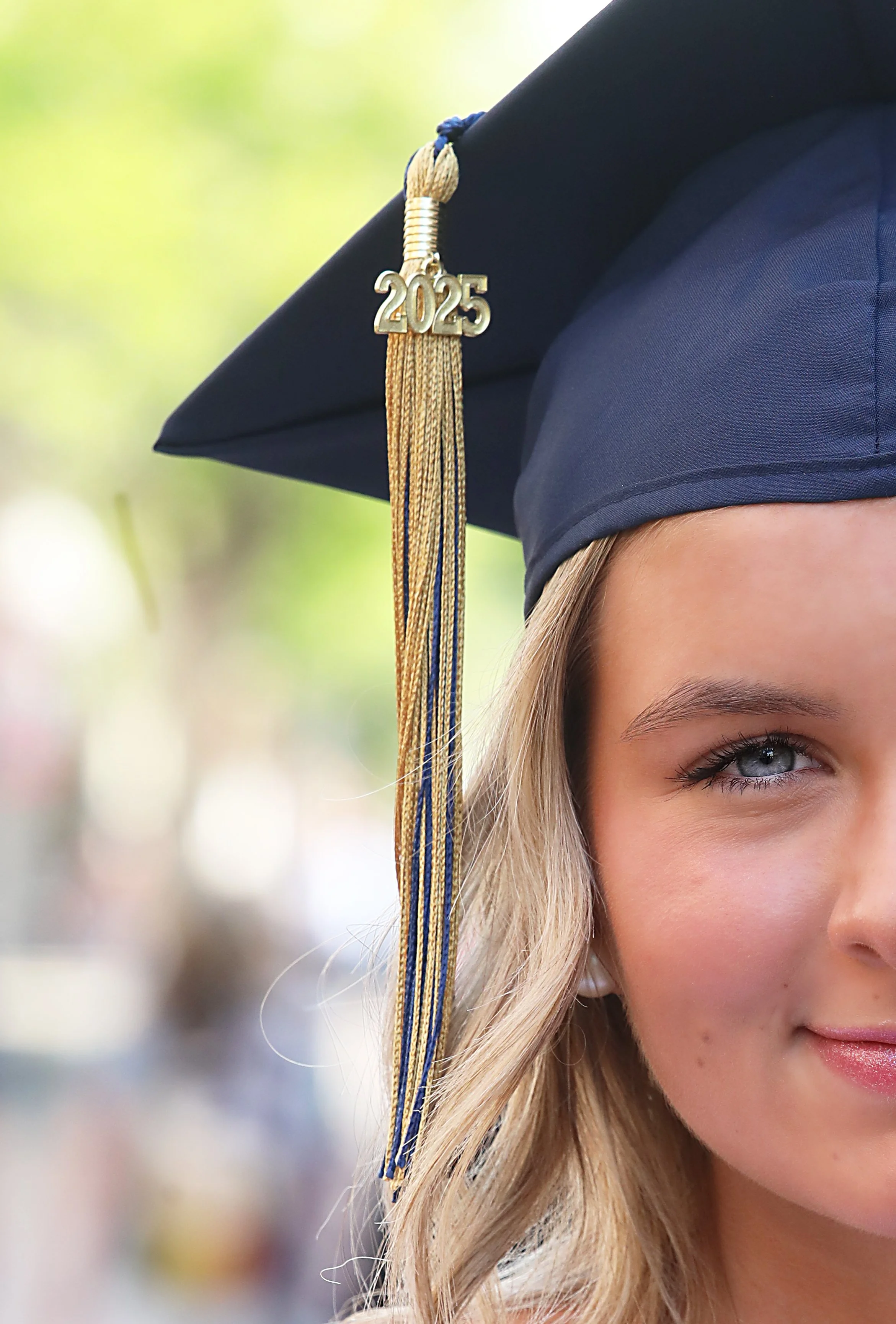 Close-up of a young woman wearing a graduation cap with a tassel marked 2025, smiling with part of her face visible.