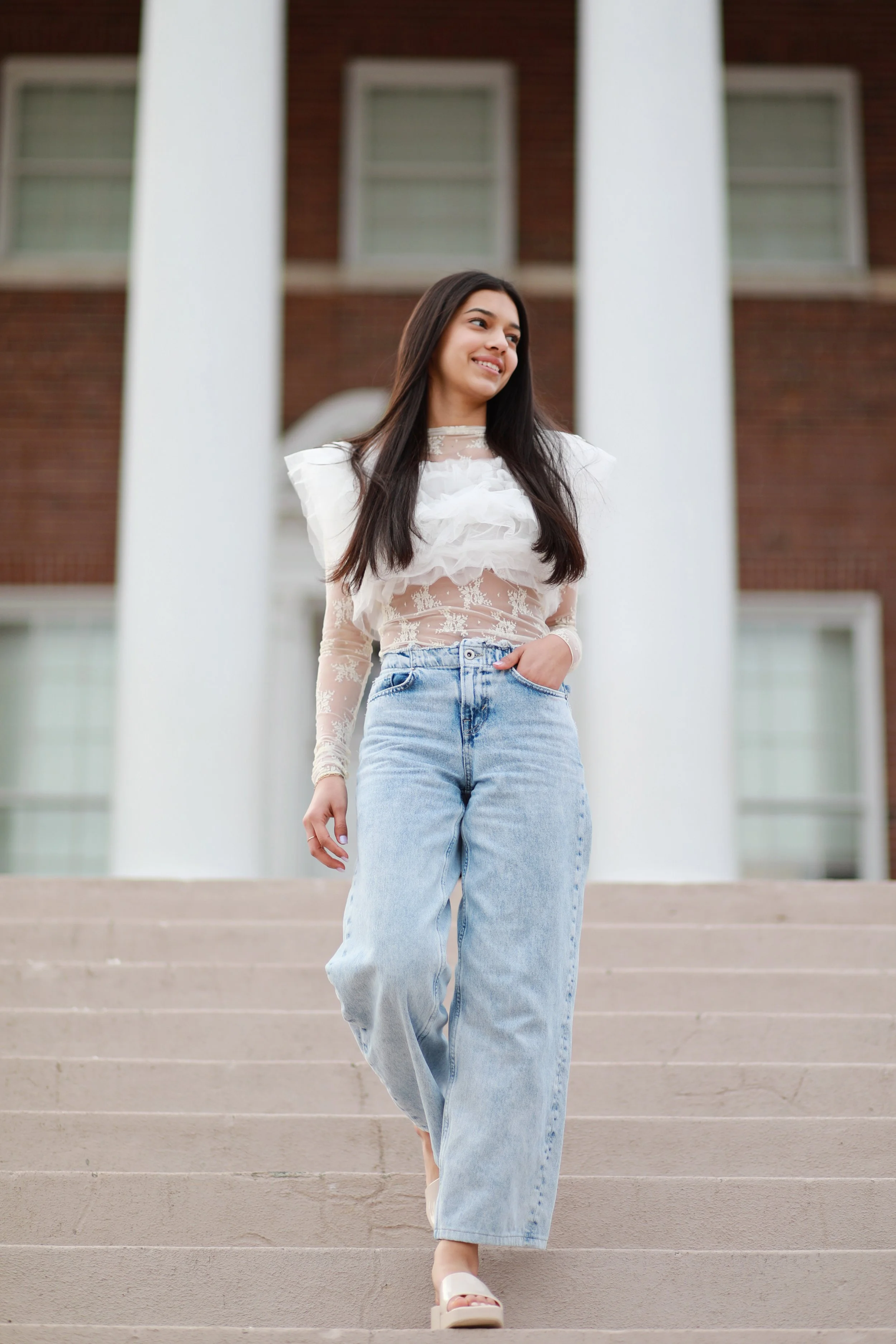 A woman is walking down stone steps outside a building with large white columns and brick walls.