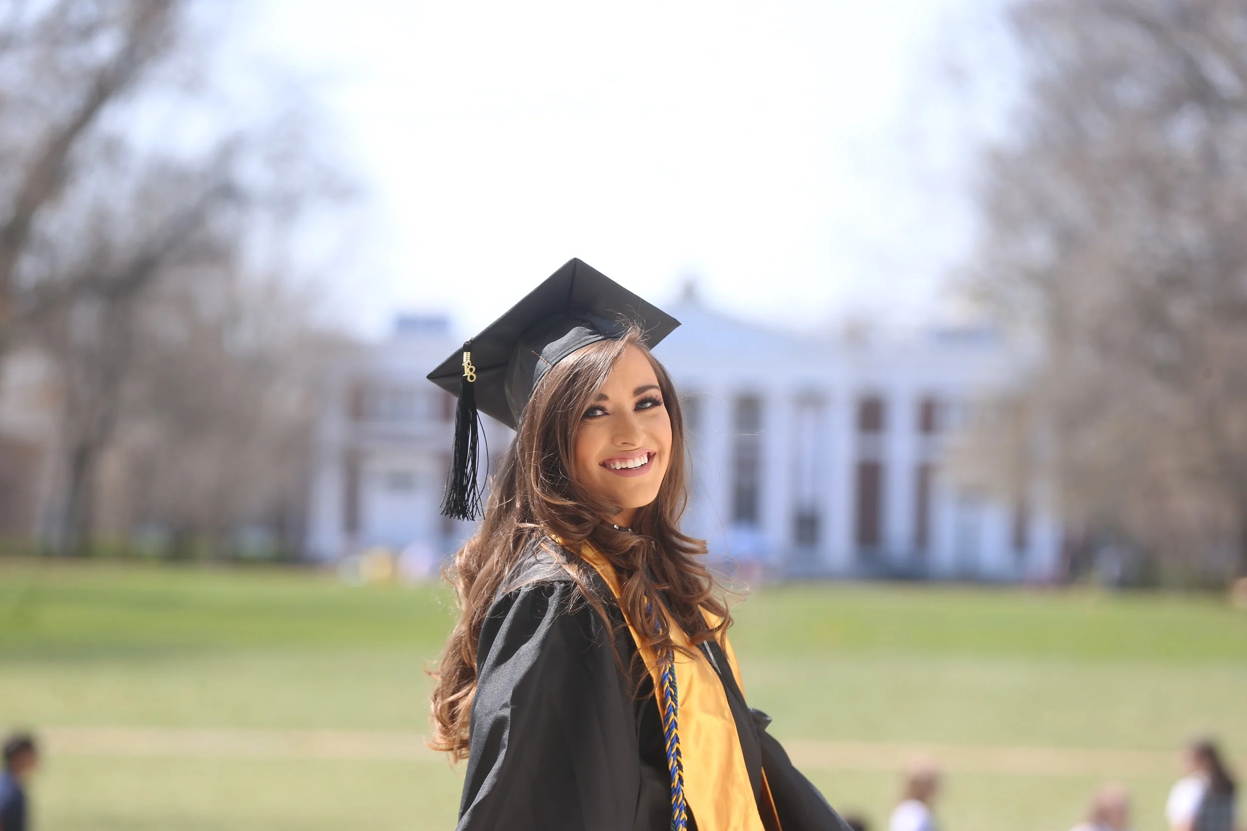 Young woman in graduation gown and cap smiling outdoors on graduation day.