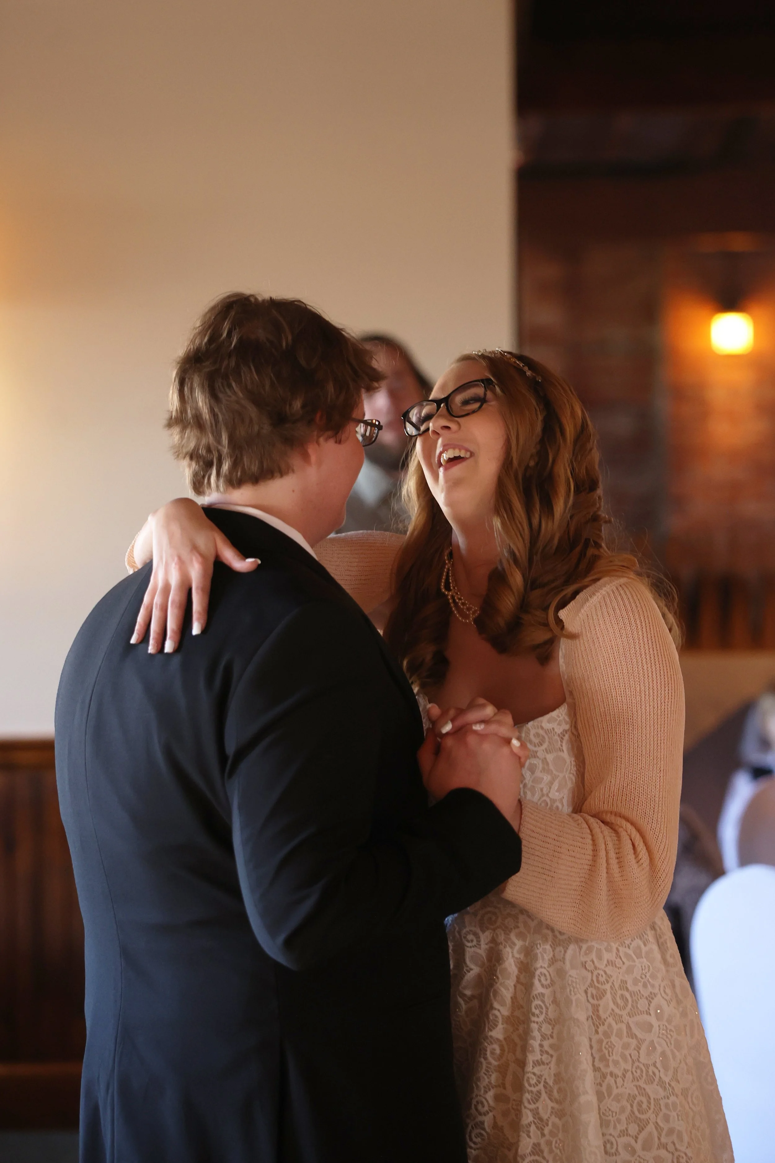 A couple dressed in formal attire dancing and smiling at each other during a wedding reception.