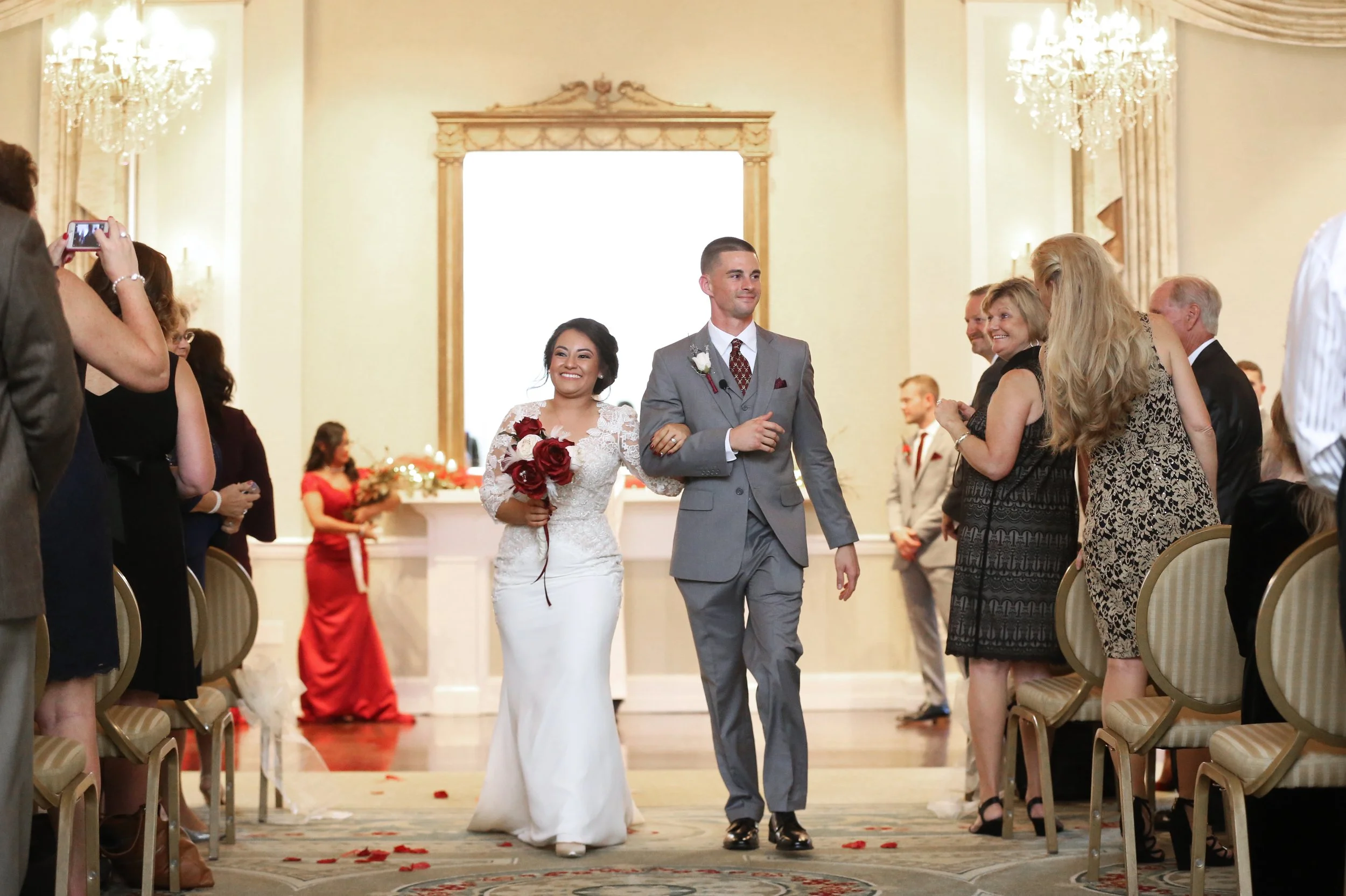 Bride and groom walk down the aisle in a wedding ceremony, surrounded by seated guests.