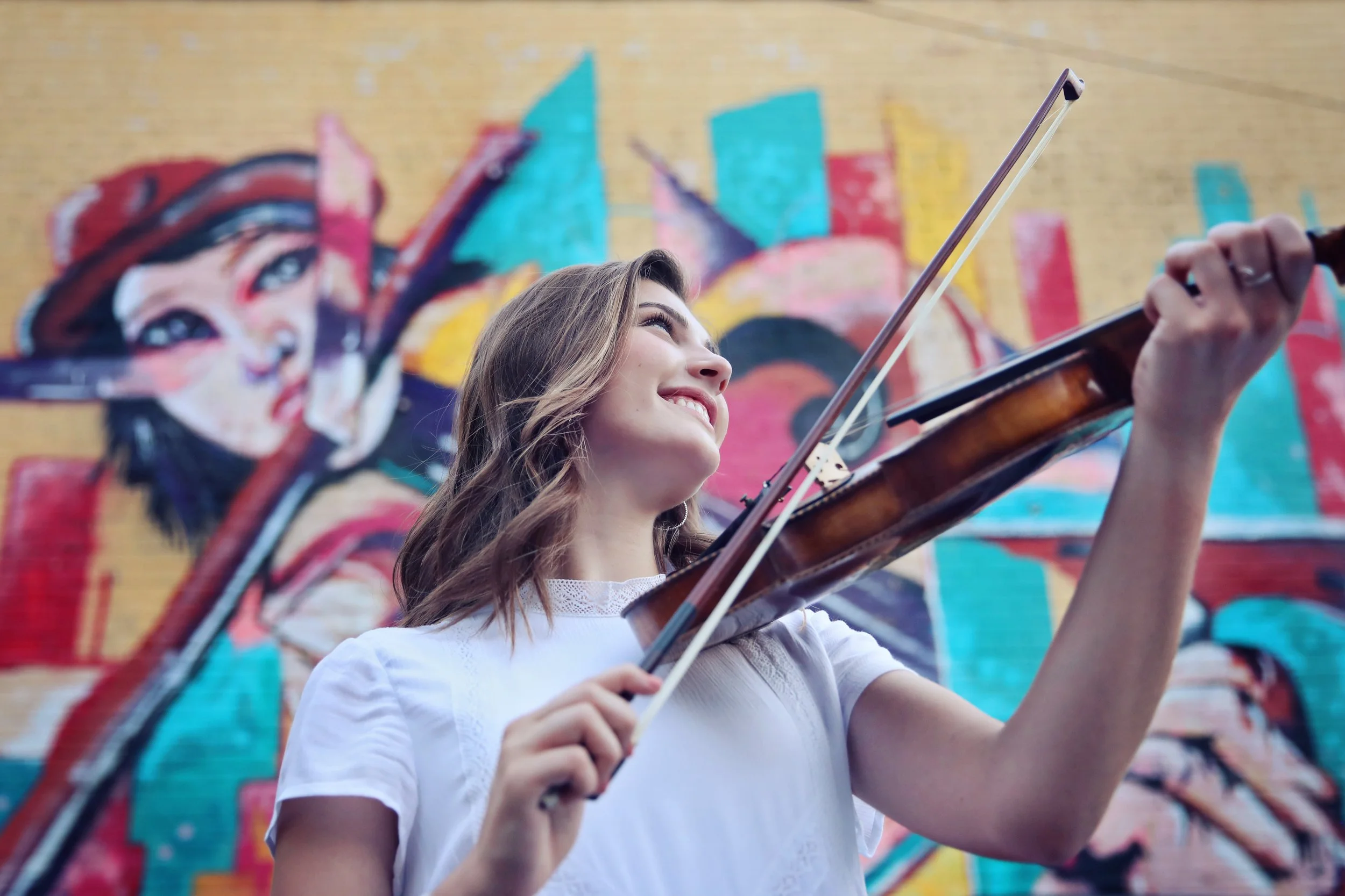 Young woman playing violin in front of colorful graffiti mural on brick wall